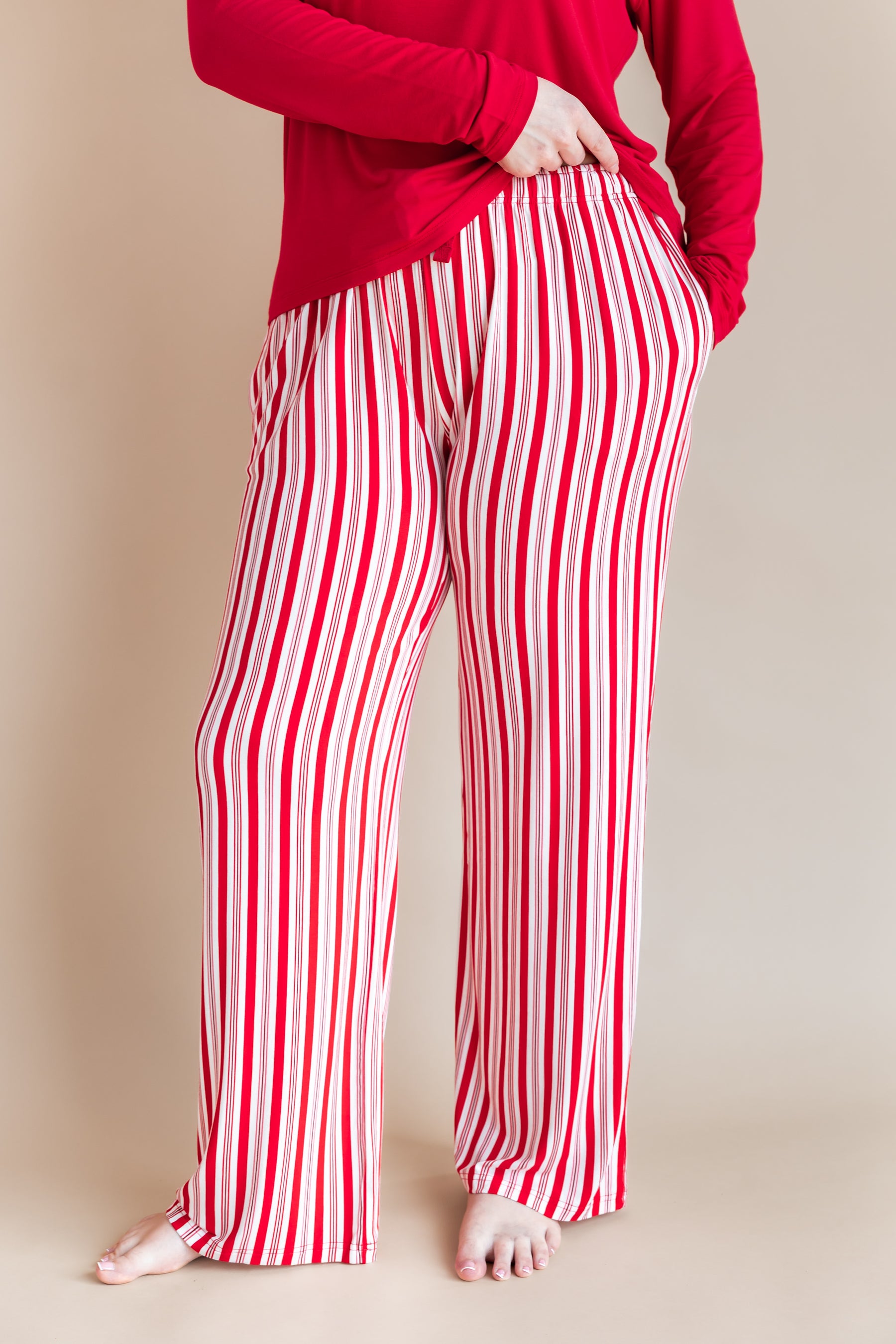 Modal wearing Women's Lounge Pants in red and white Peppermint Stripes print under a red T-shirt on a beige background