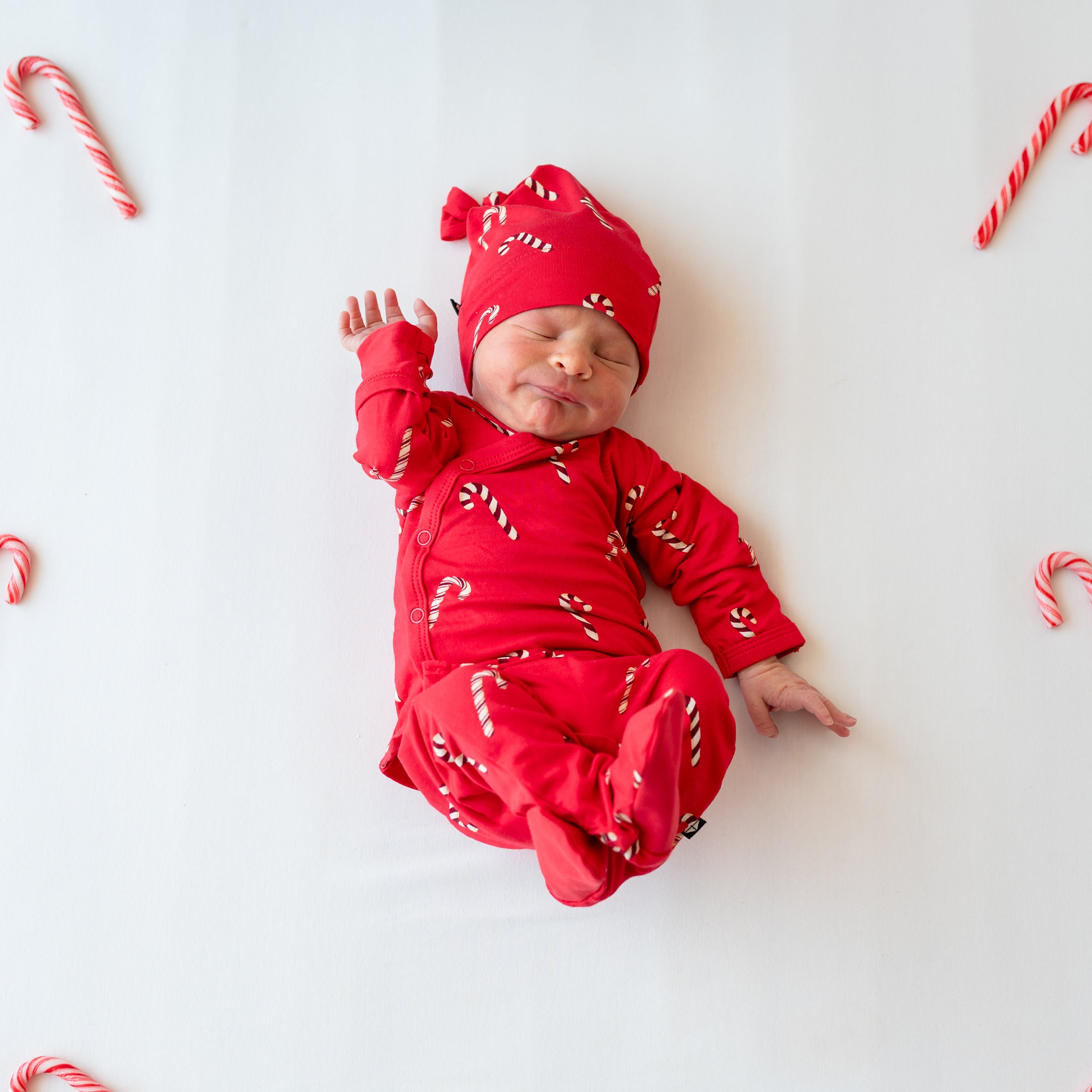 Sleeping newborn wearing the Take Me Home Set with Cap in Candy Cane laying down on a white blanket with candy canes around them