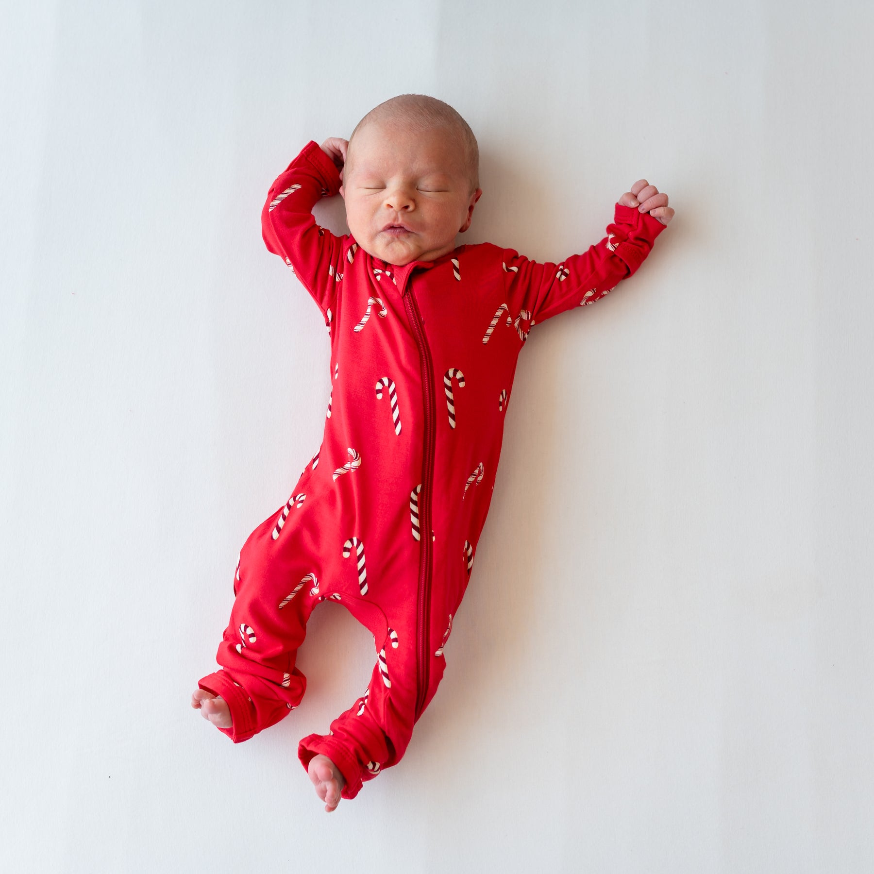 Sleeping newborn laying down wearing the Zippered Romper in Candy Cane on a white blanket