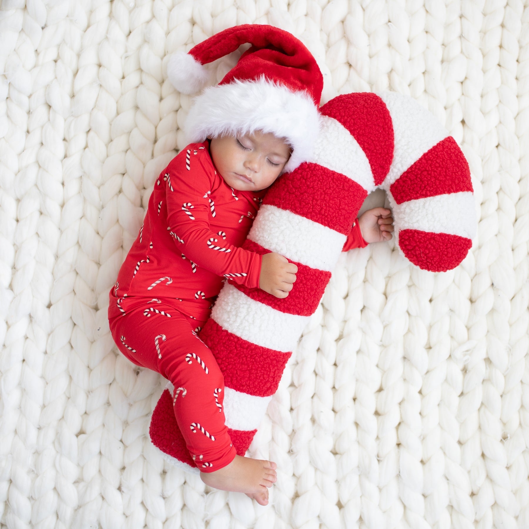 Sleeping toddler wearing the Long Sleeve Pajamas in Candy Cane holding a stuffed Candy Cane and wearing a Santa Hat