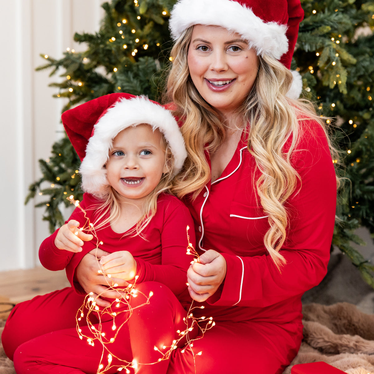 Mom and daughter wearing matching red pajamas with christmas decor and tree 