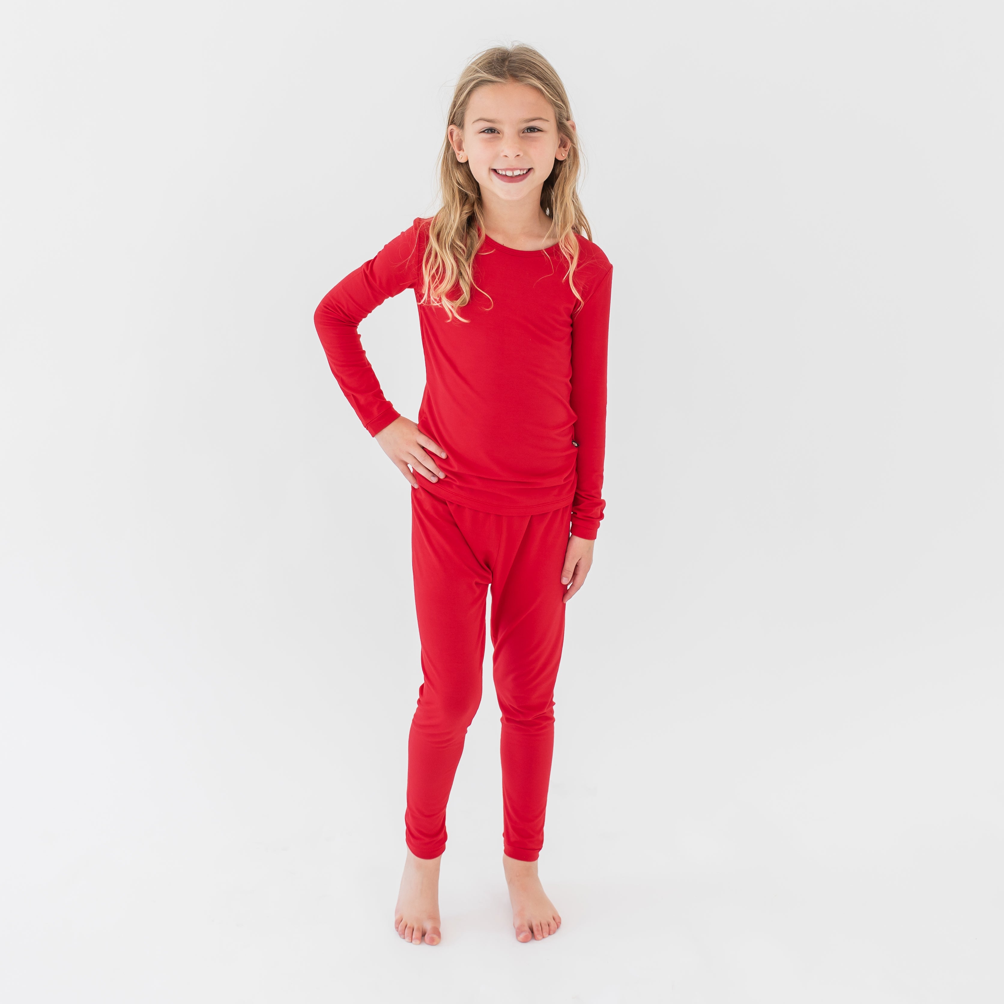 Young model standing with a hand on her hip wearing the Long Sleeve Pajamas in Cardinal in front of a white background