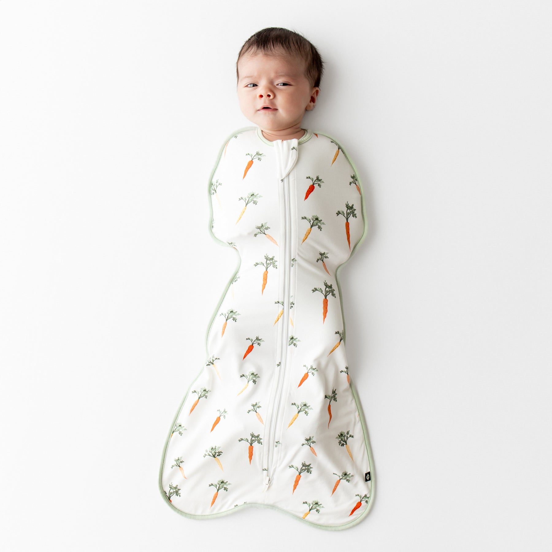 Newborn laying on a white surface wearing the Swaddle Bag in Carrot 0.5