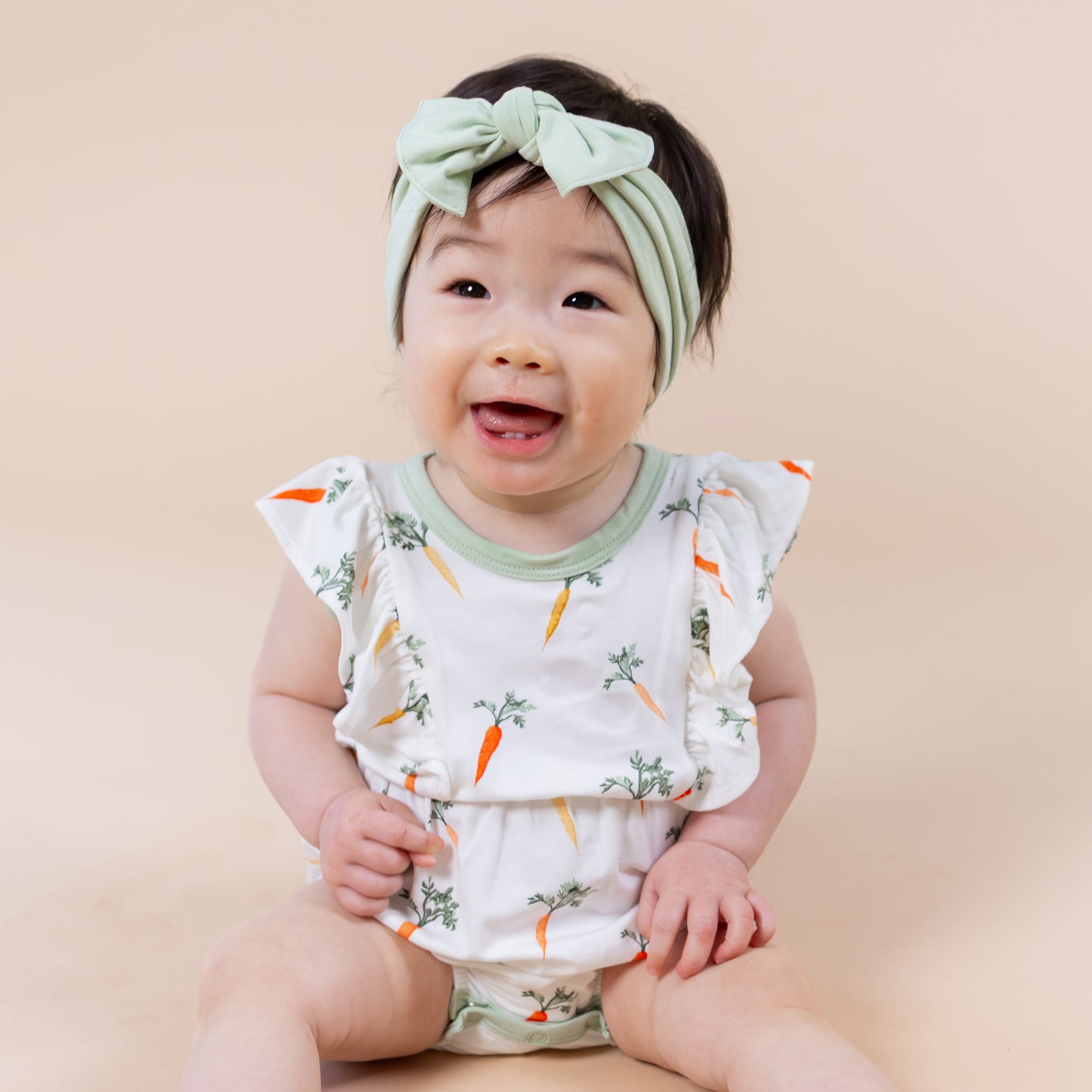 Close up of smiling toddler wearing the Bubble Romper in Carrot with green bow in her hair