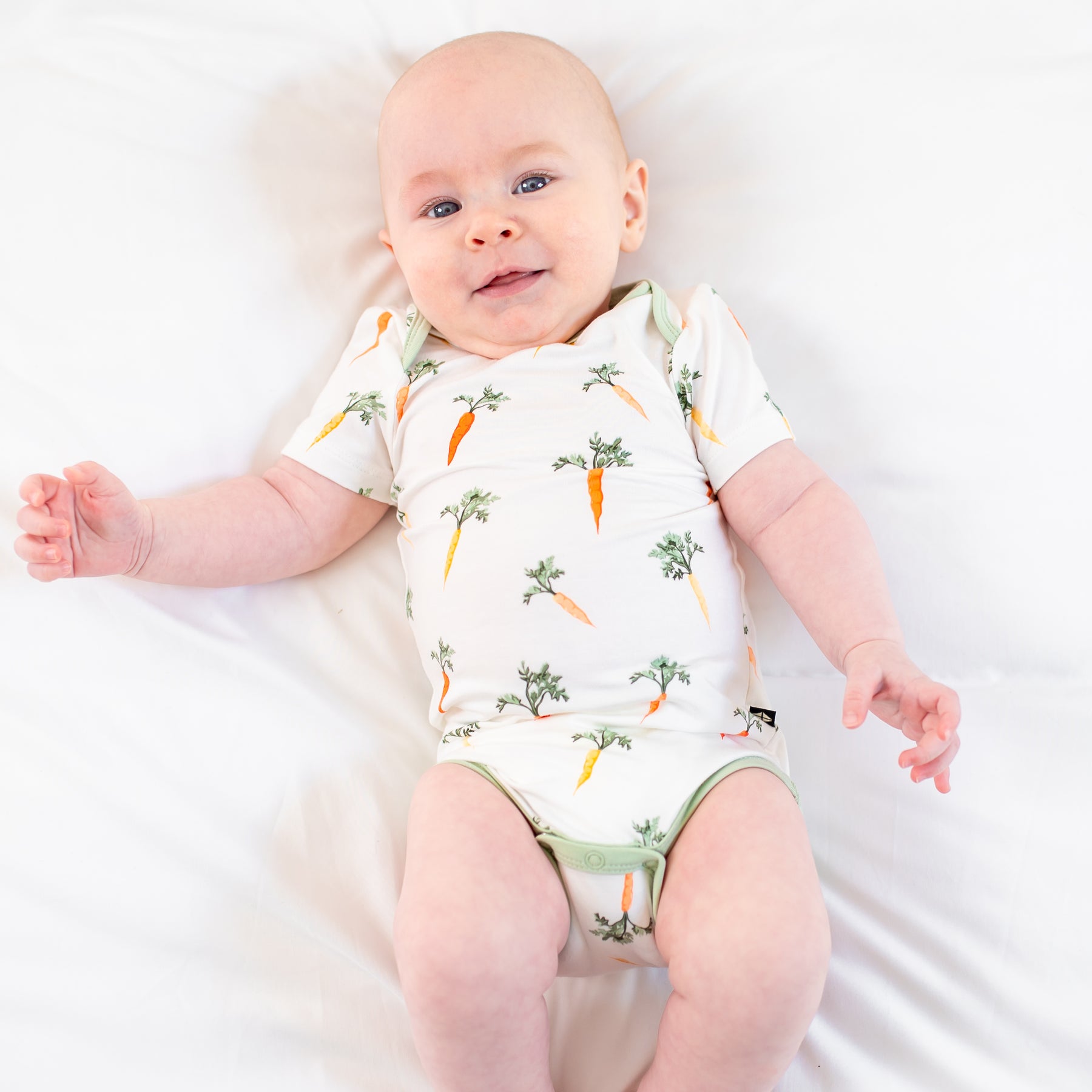 Infant laying in a bed wearing the Bodysuit in Carrot