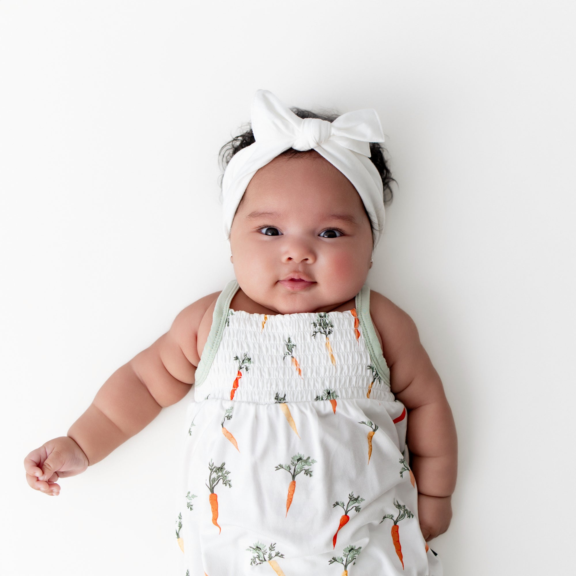 Close up of infant wearing the Smocked Bubble Romper in Carrot with a white bow