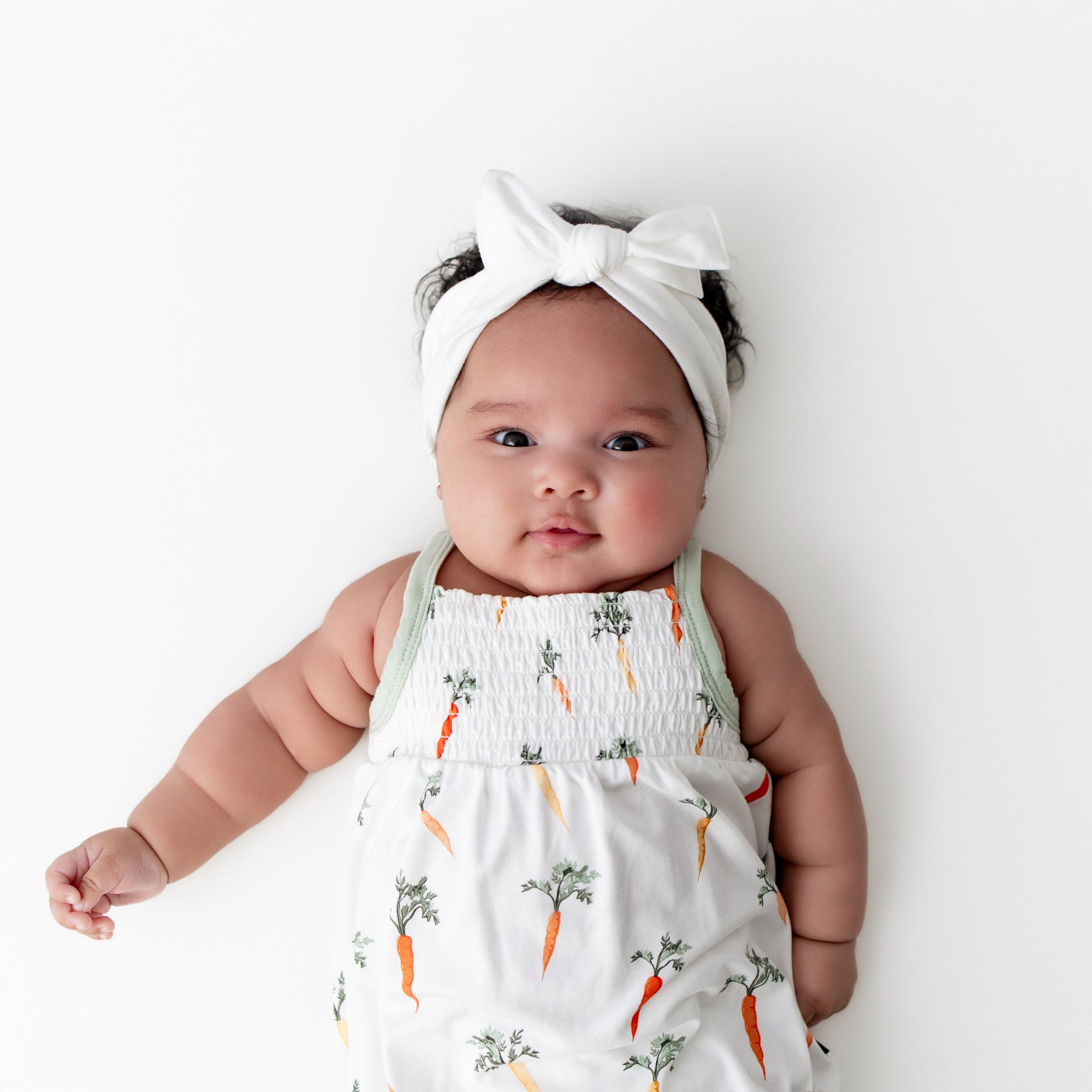 Close up of infant wearing the Smocked Bubble Romper in Carrot with a white bow