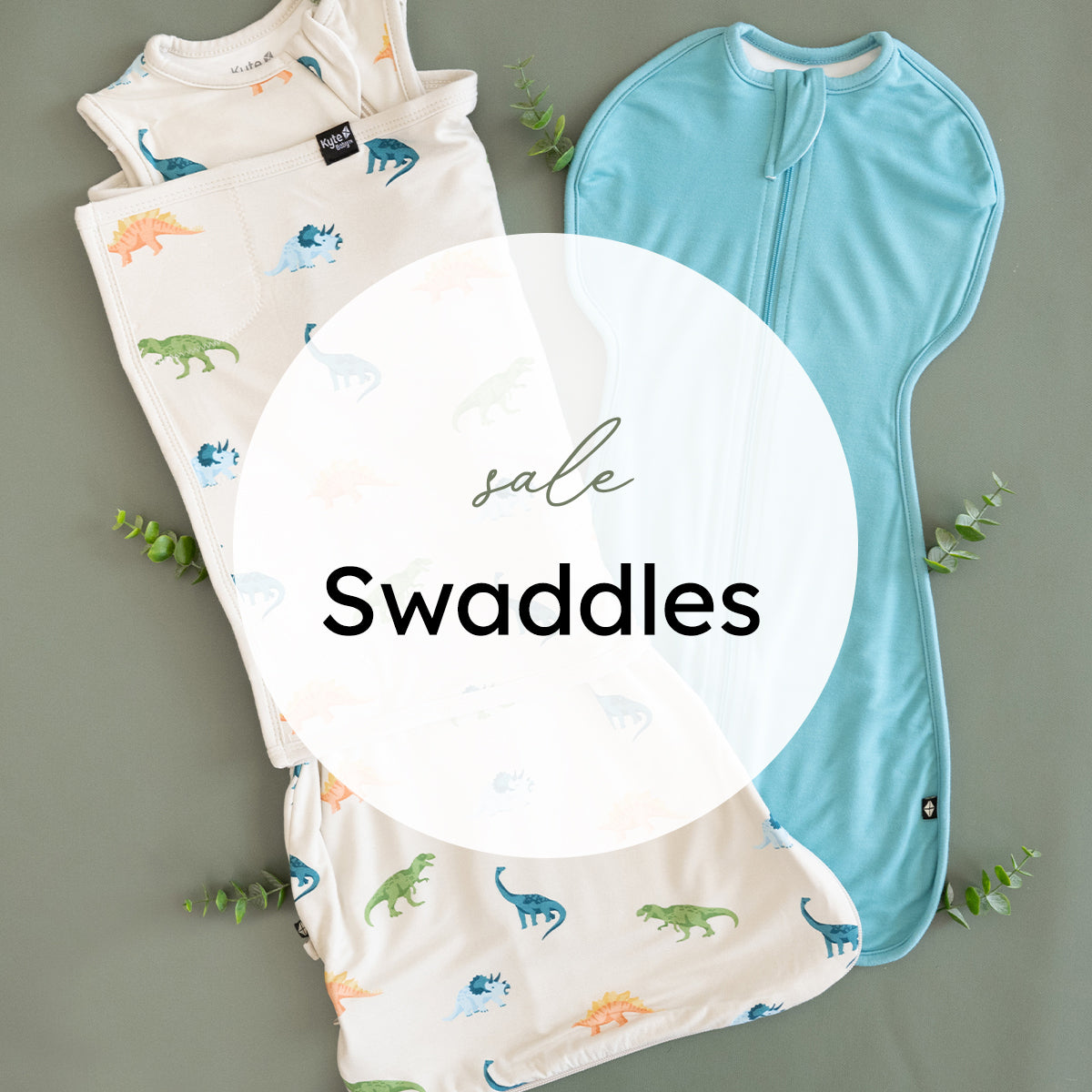 Three baby swaddles laid flat on a muted green-gray background with small greenery accents. One swaddle is light aqua blue, and two are cream with colorful dinosaur prints in blue, green, orange, and teal.