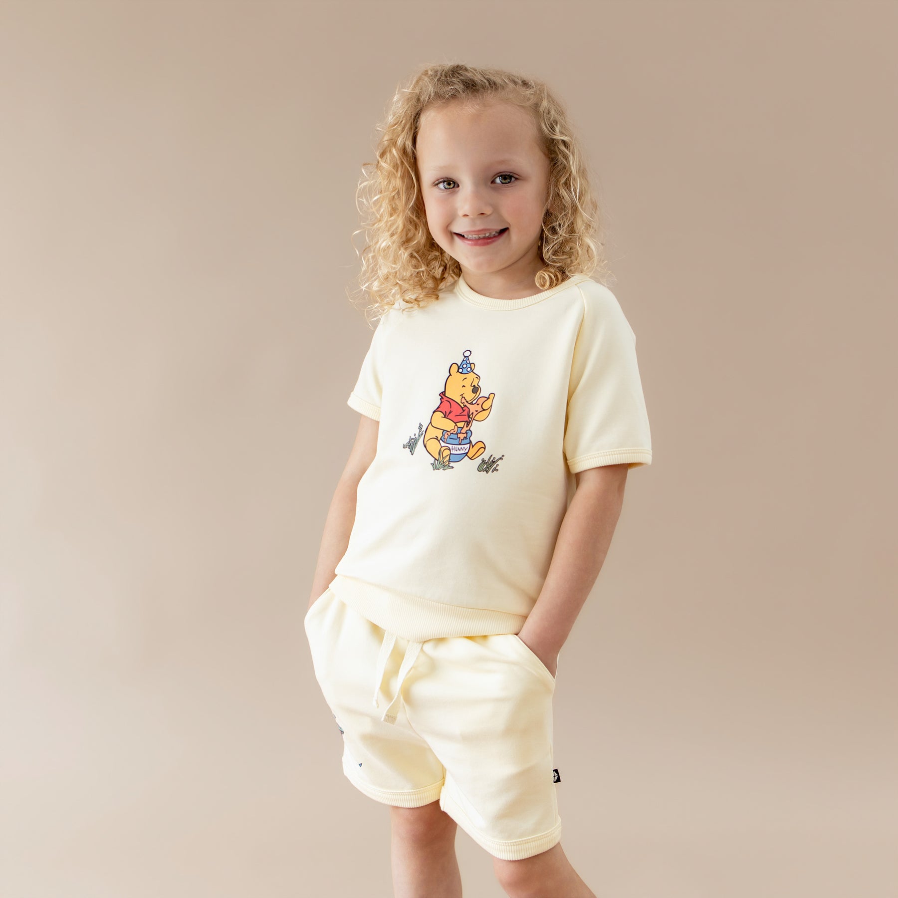 Young girl modeling the Short Sleeve Jogger Set in Winnie the Pooh on Chamomile with the hands in the pockets of the shorts