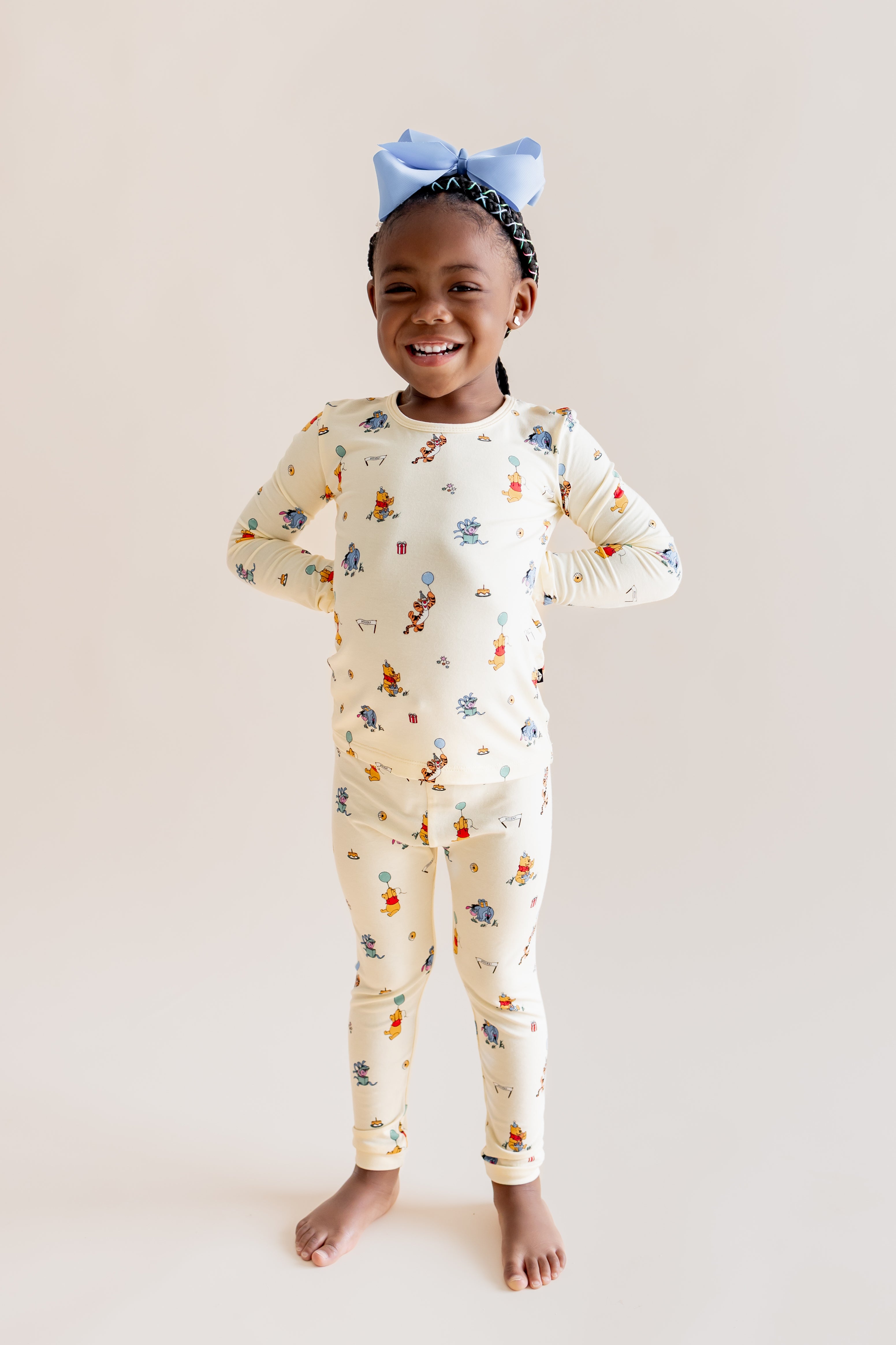 Girl posing in Long Sleeve Pajamas in Winnie the Pooh Celebration print on a beige background