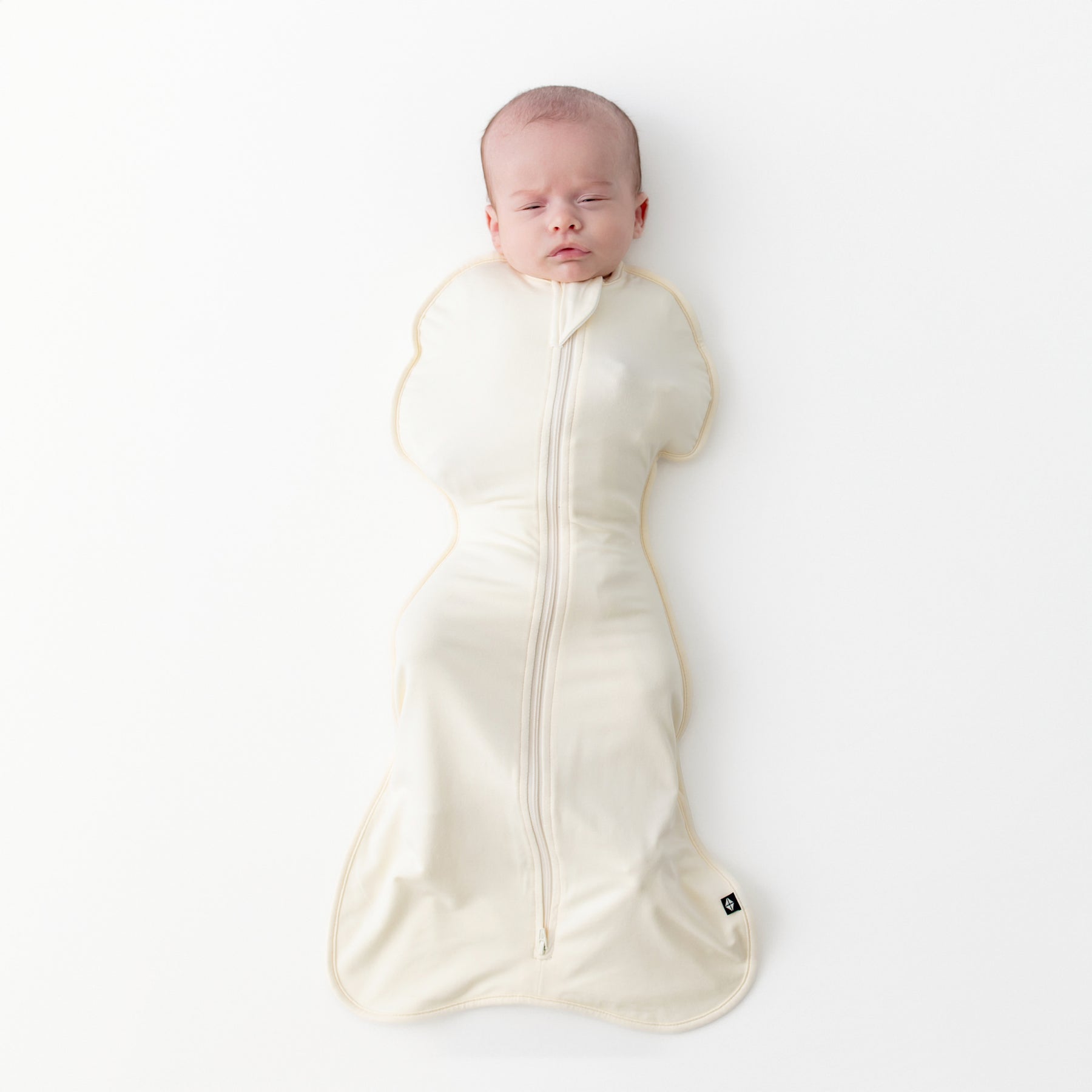 Newborn laying on a light neutral surface wearing the Swaddle Bag in Chamomile 0.5