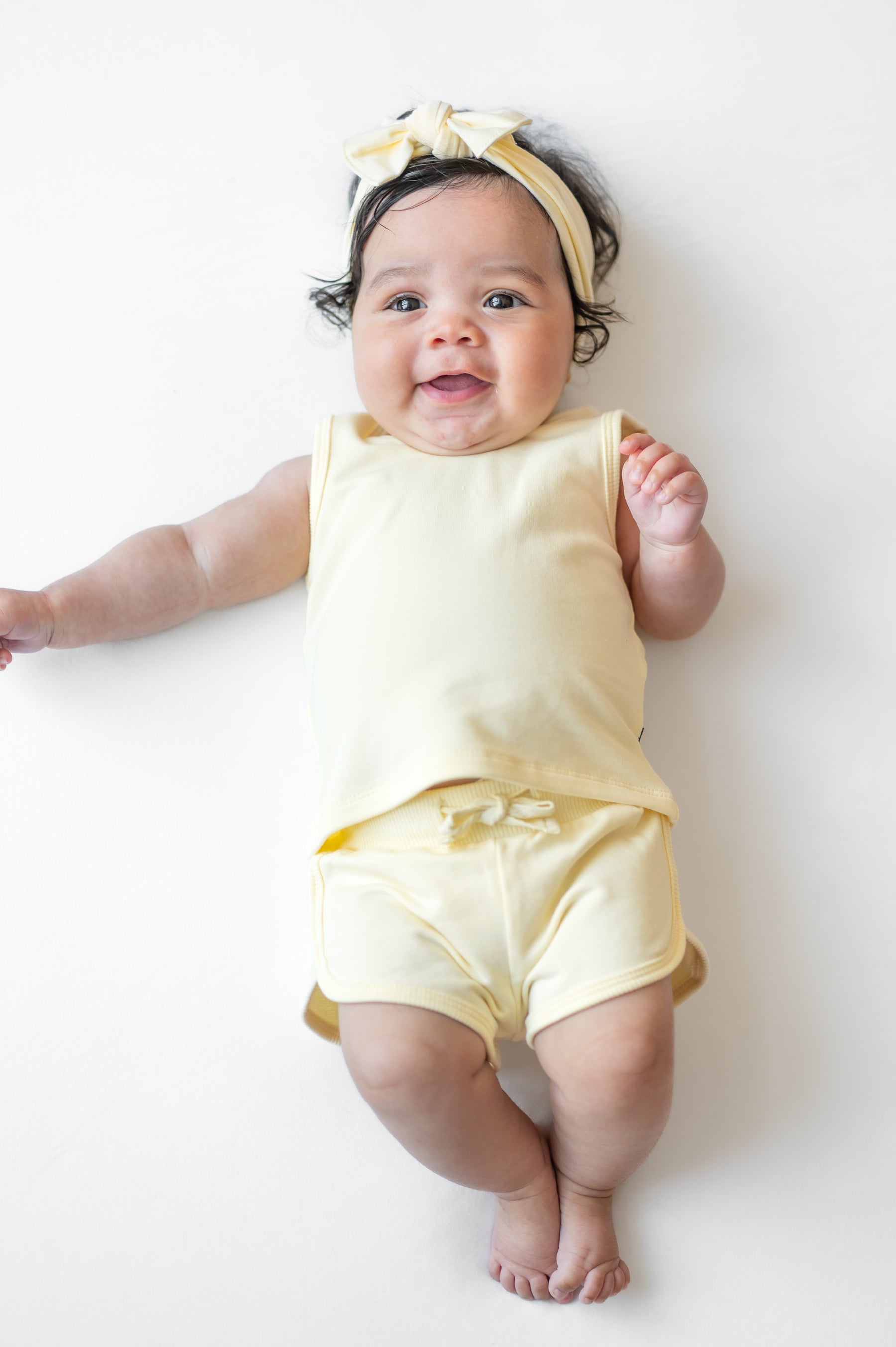 Infant laying on a white surface wearing the Tank Jogger Set in Chamomile with a matching bow