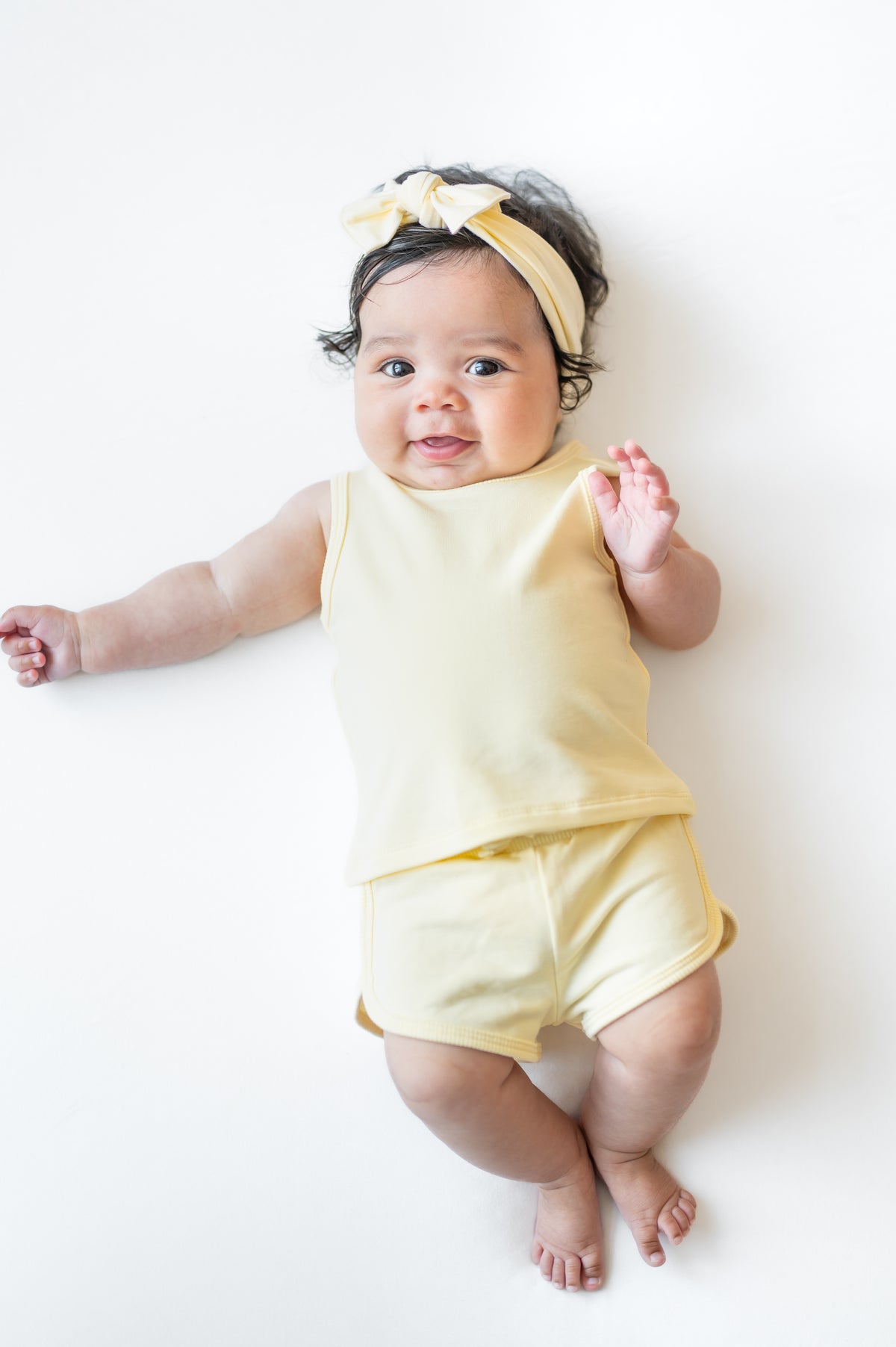Infant laying on a white surface wearing the Tank Jogger Set in Chamomile with a matching bow