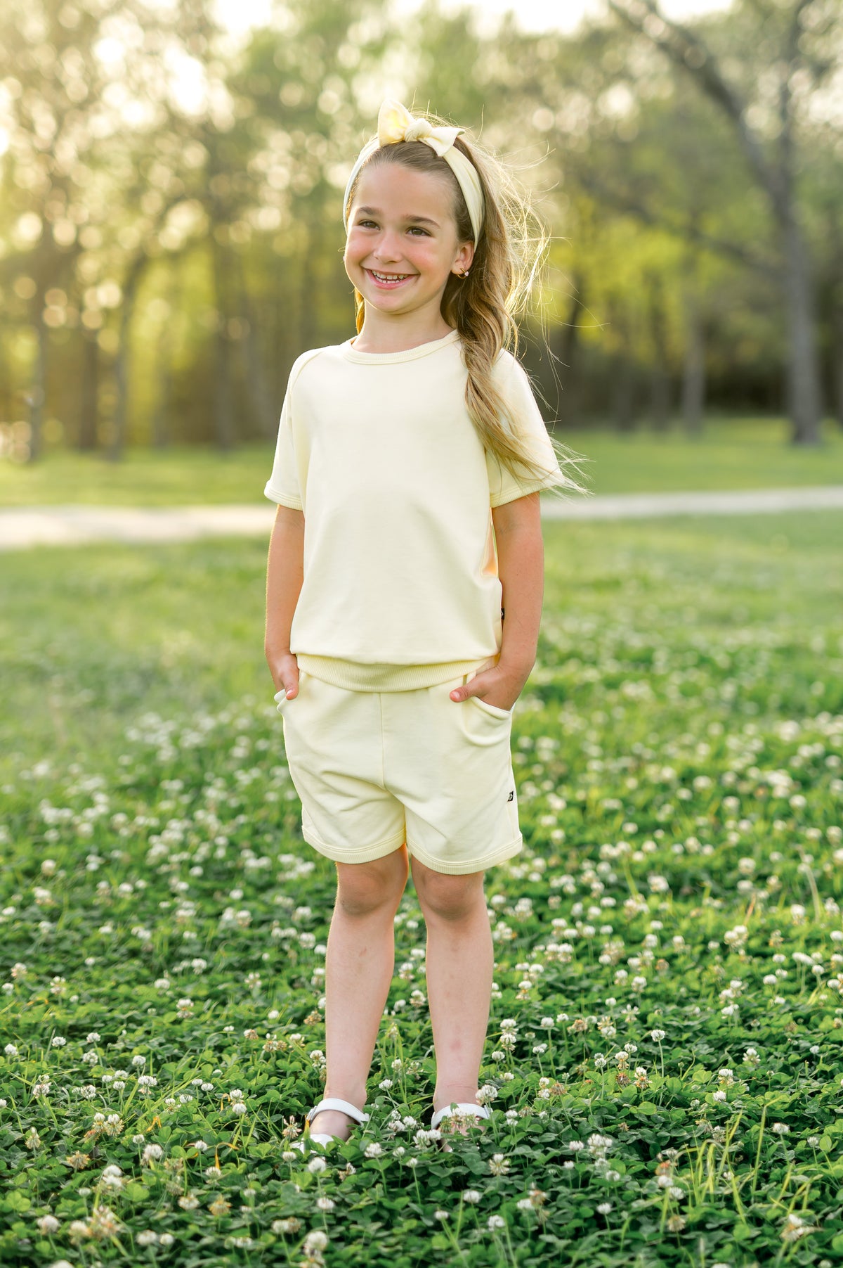 Young girl standing in a grass field wearing the Short Sleeve Jogger Set in Chamomile with hands in the shorts pocket