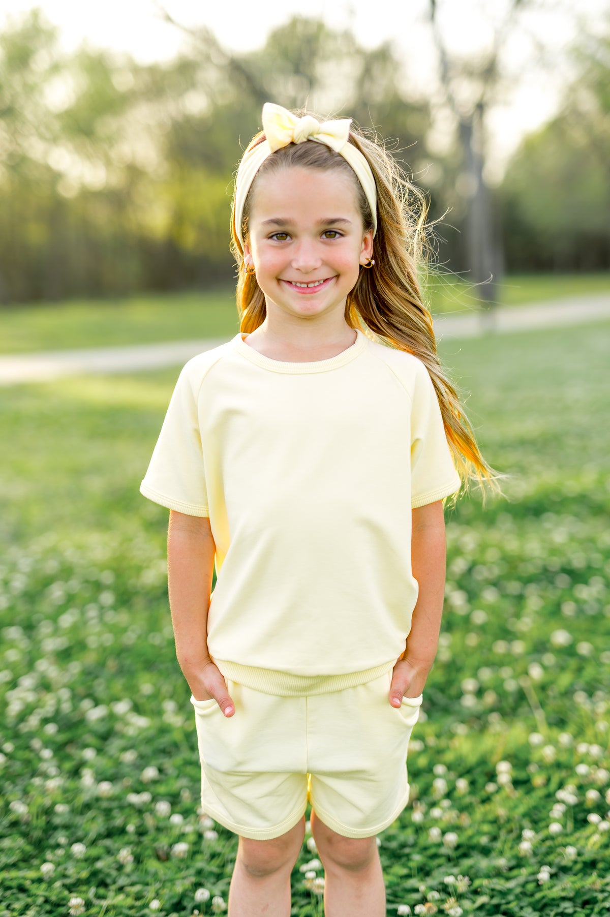 Close up of the a young girl standing in a field wearing the Short Sleeve Jogger Set in Chamomile
