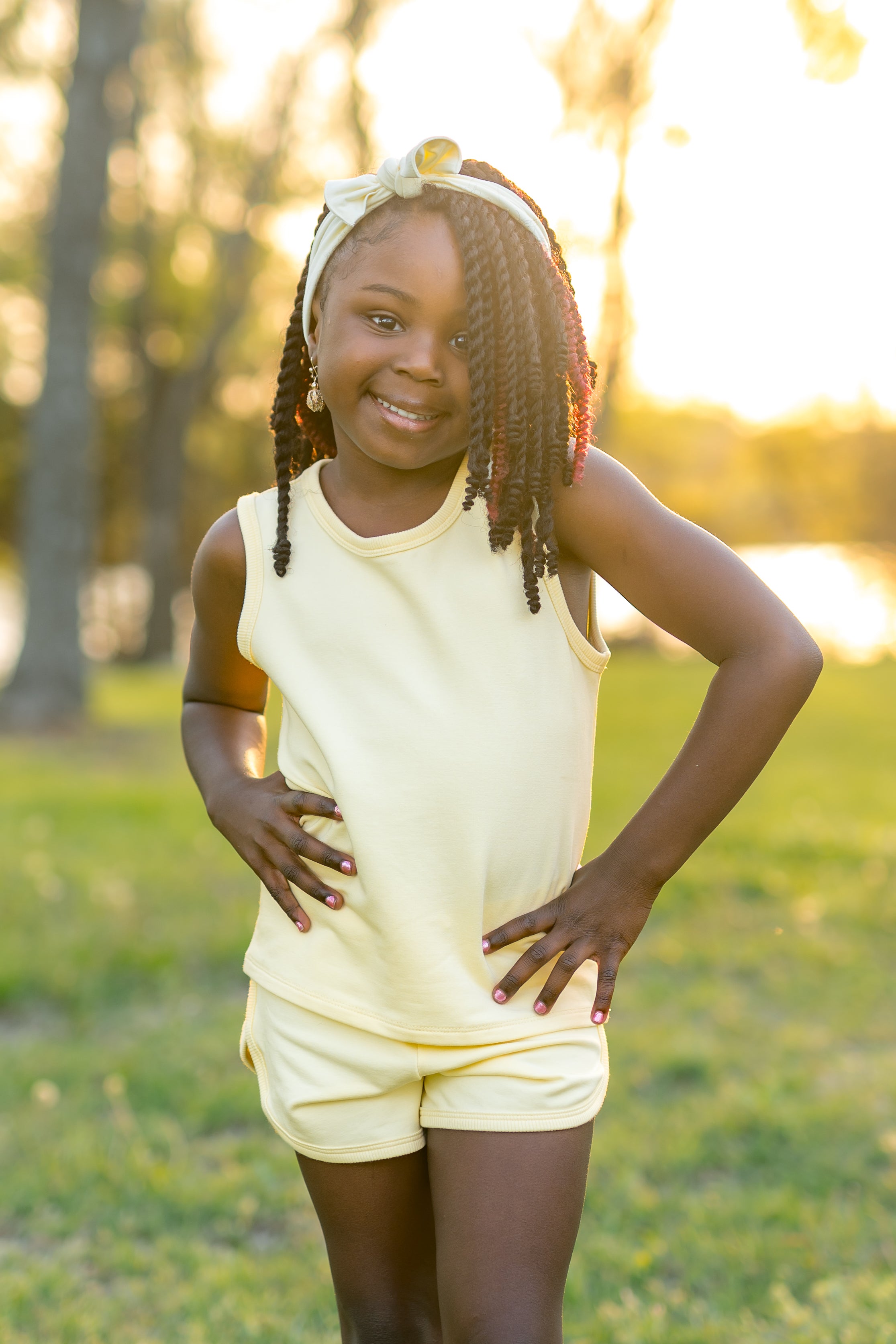 Young girl posing wearing the Tank Jogger Set in Chamomile in front of a sun set in a grass field