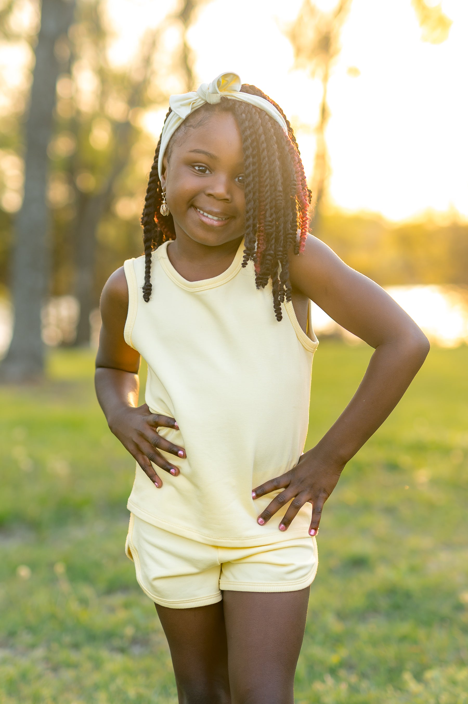 Young girl posing wearing the Tank Jogger Set in Chamomile in front of a sun set in a grass field