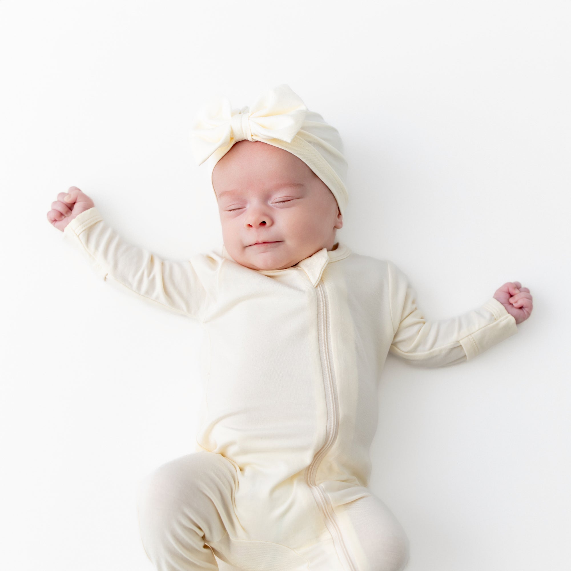 Sleeping newborn wearing the Bow Headwrap Chamomile with matching zippered romper