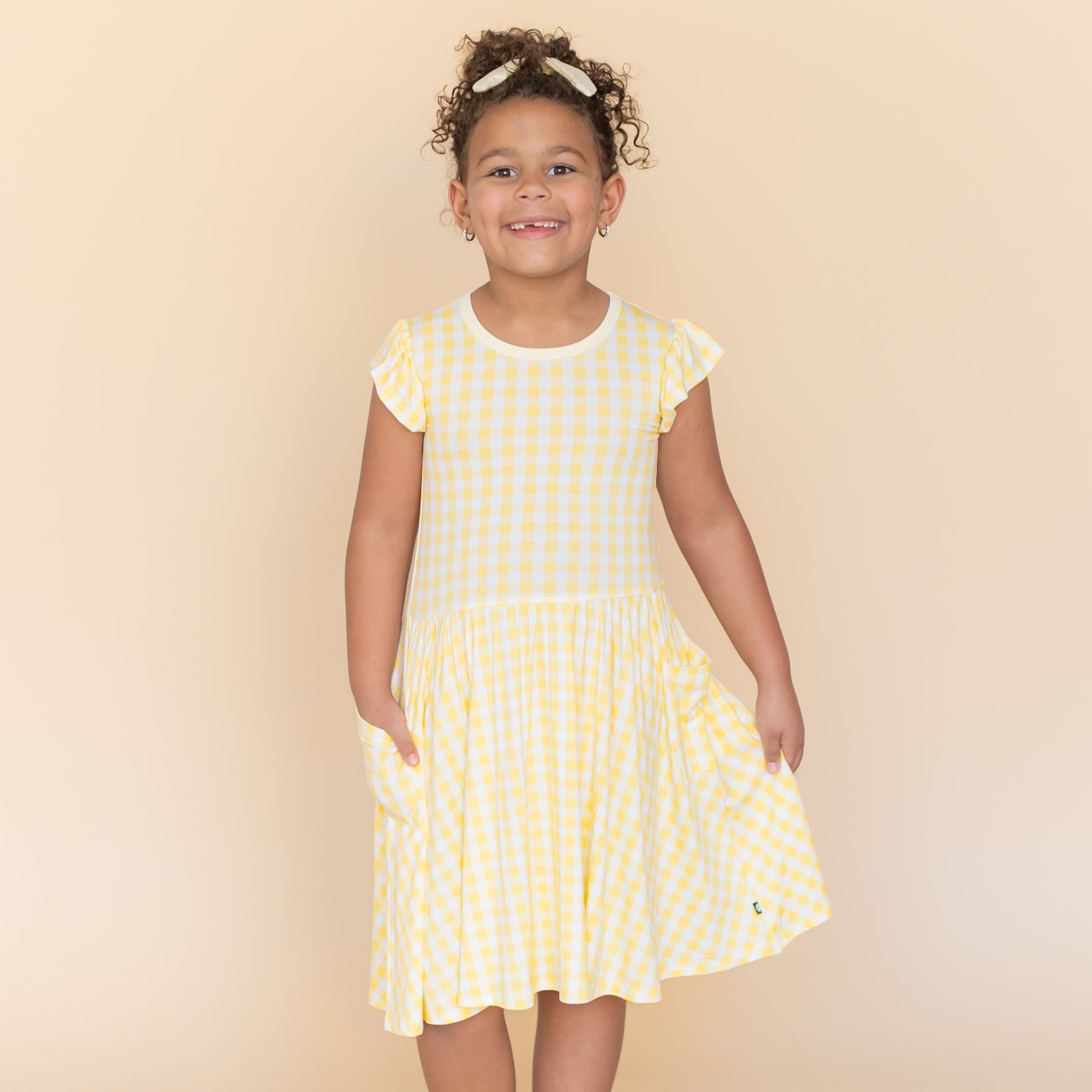 Young girl modeling the Pocket Dress in Gingham Chamomile with one hand in the pocket with the other hand holding the skirt of the dress