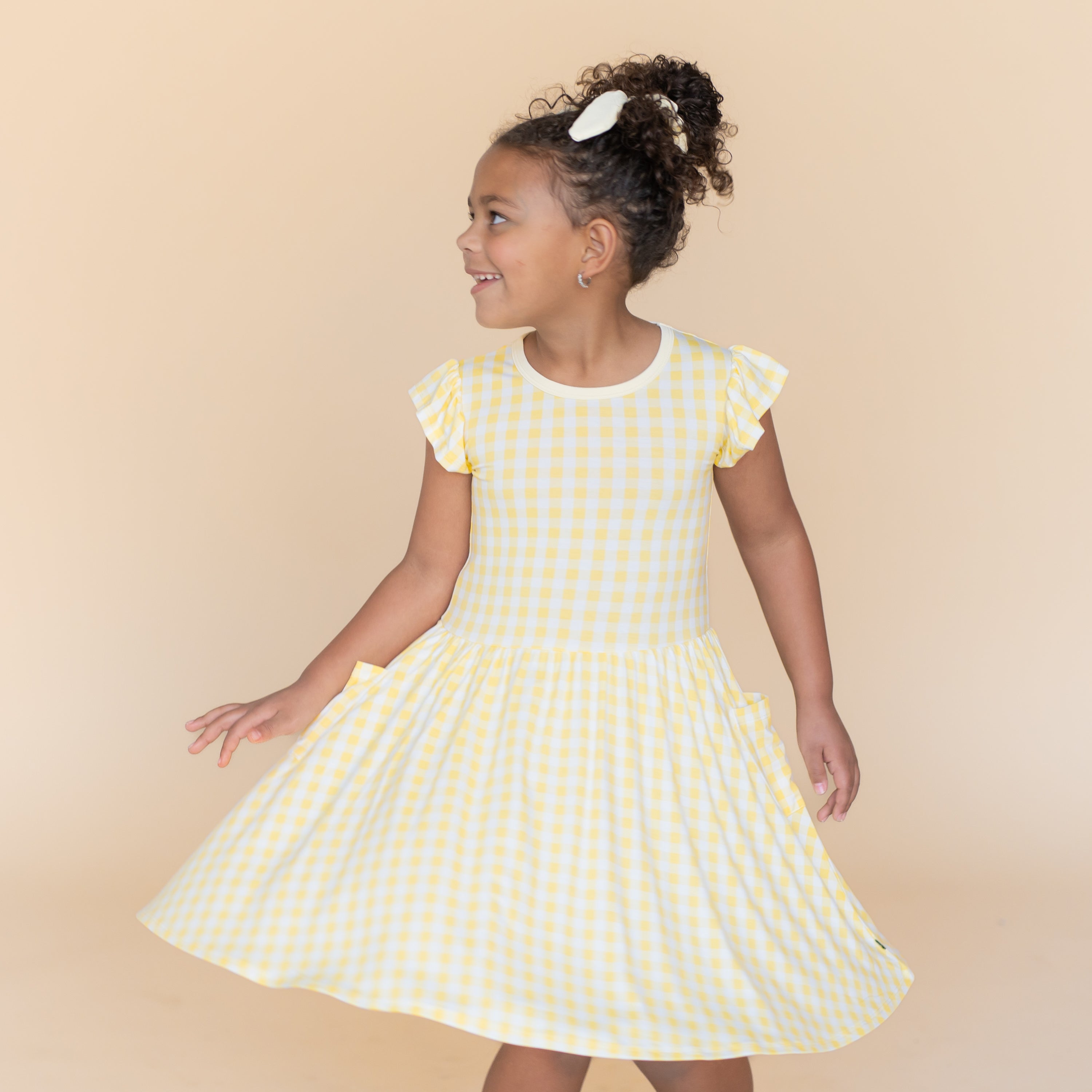 Young girl twirling wearing the Pocket Dress in Gingham Chamomile