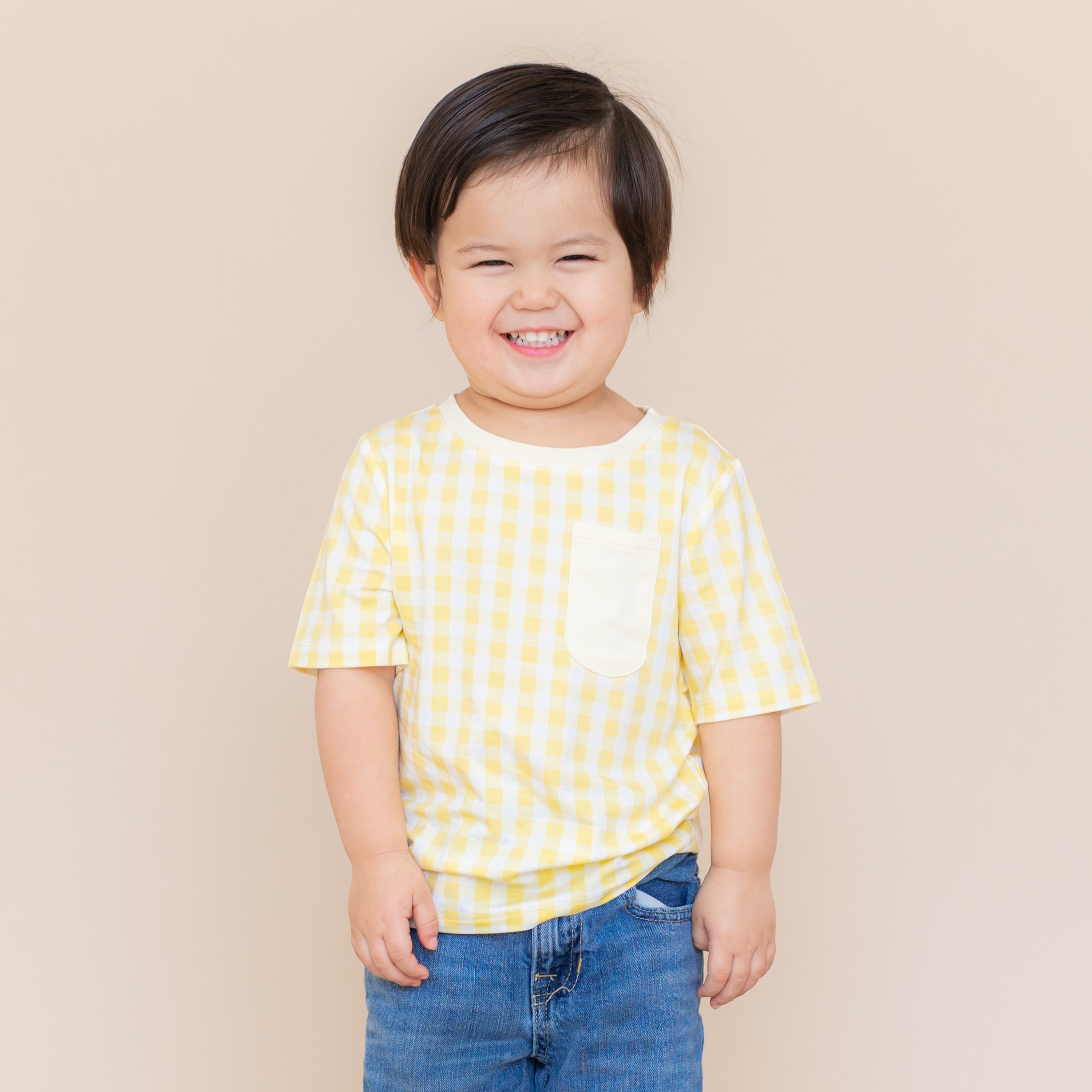 Smiling child wearing the Toddler Crew Neck Tee in Gingham Chamomile with medium wash jeans