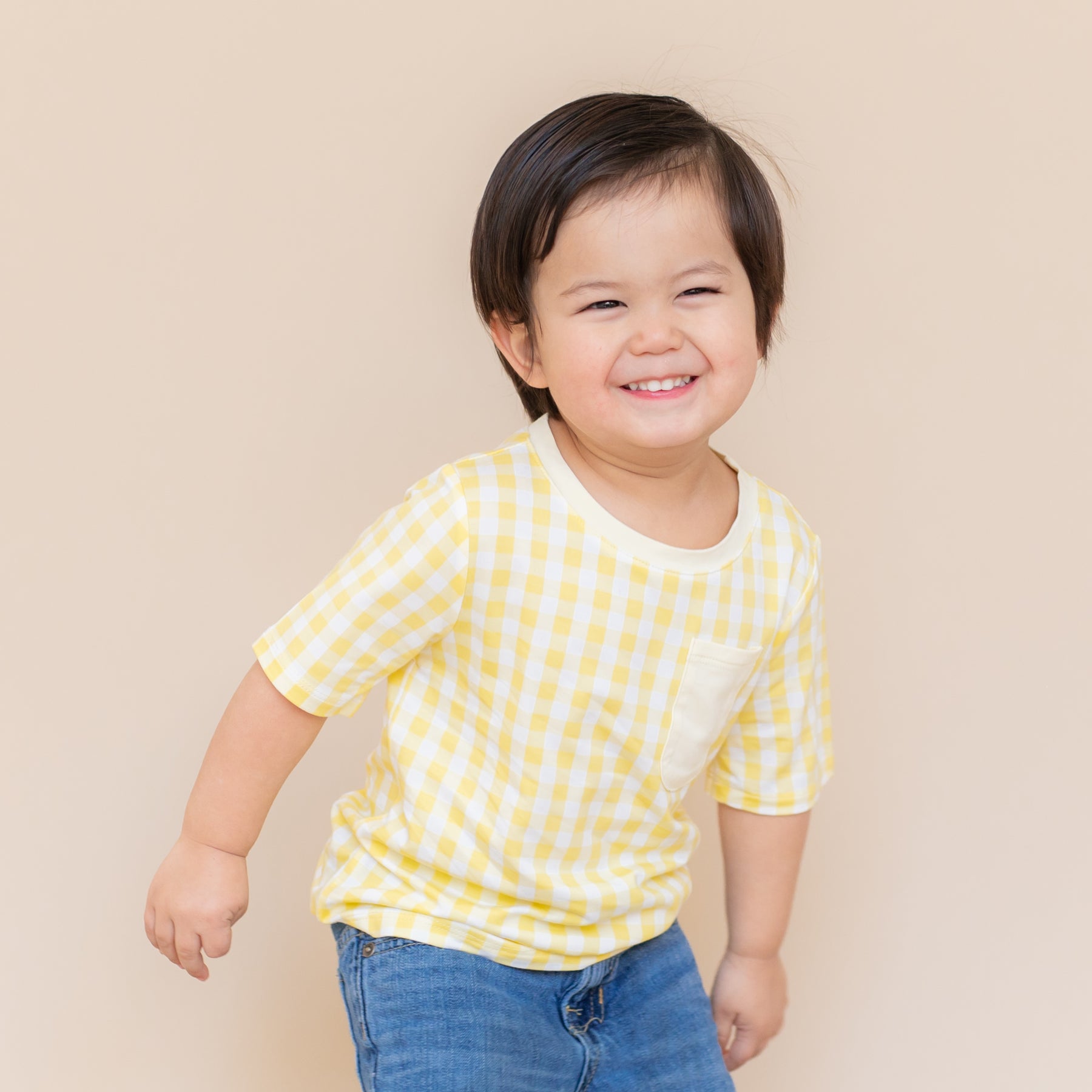 Young smiling child wearing the Toddler Crew Neck Tee in Gingham Chamomile with medium wash jeans