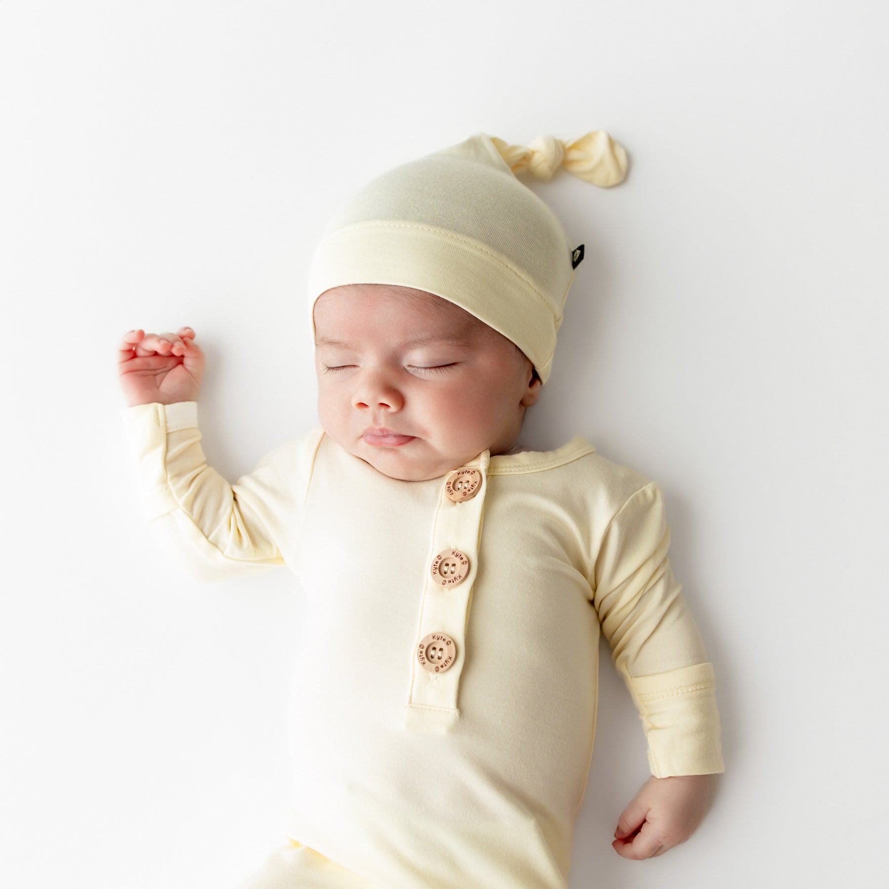 Baby wearing a light yellow-colored outfit with buttons and a matching hat on a white background