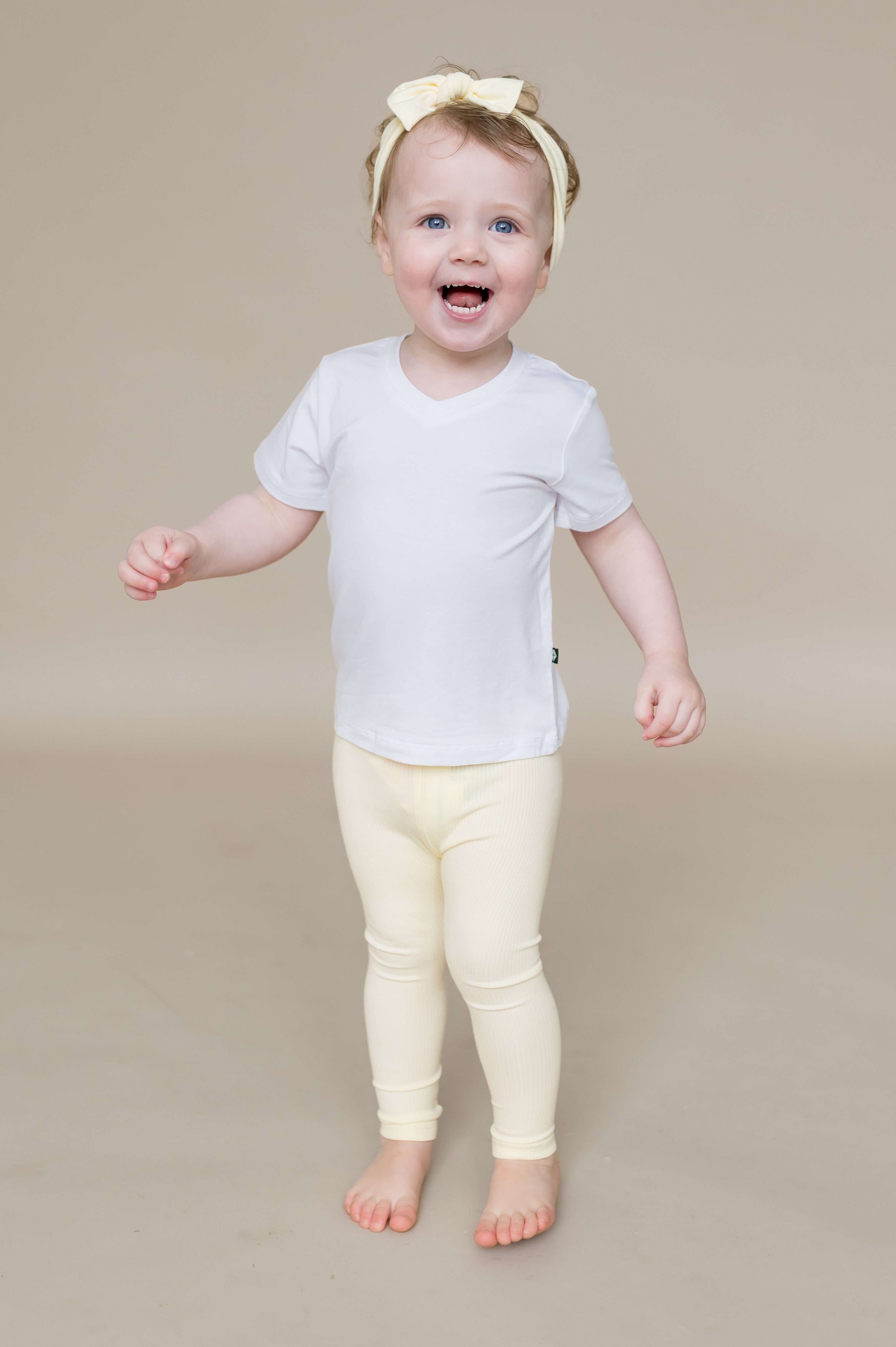 Smiling toddler wearing the Ribbed Leggings in Chamomile paired with a white v-neck