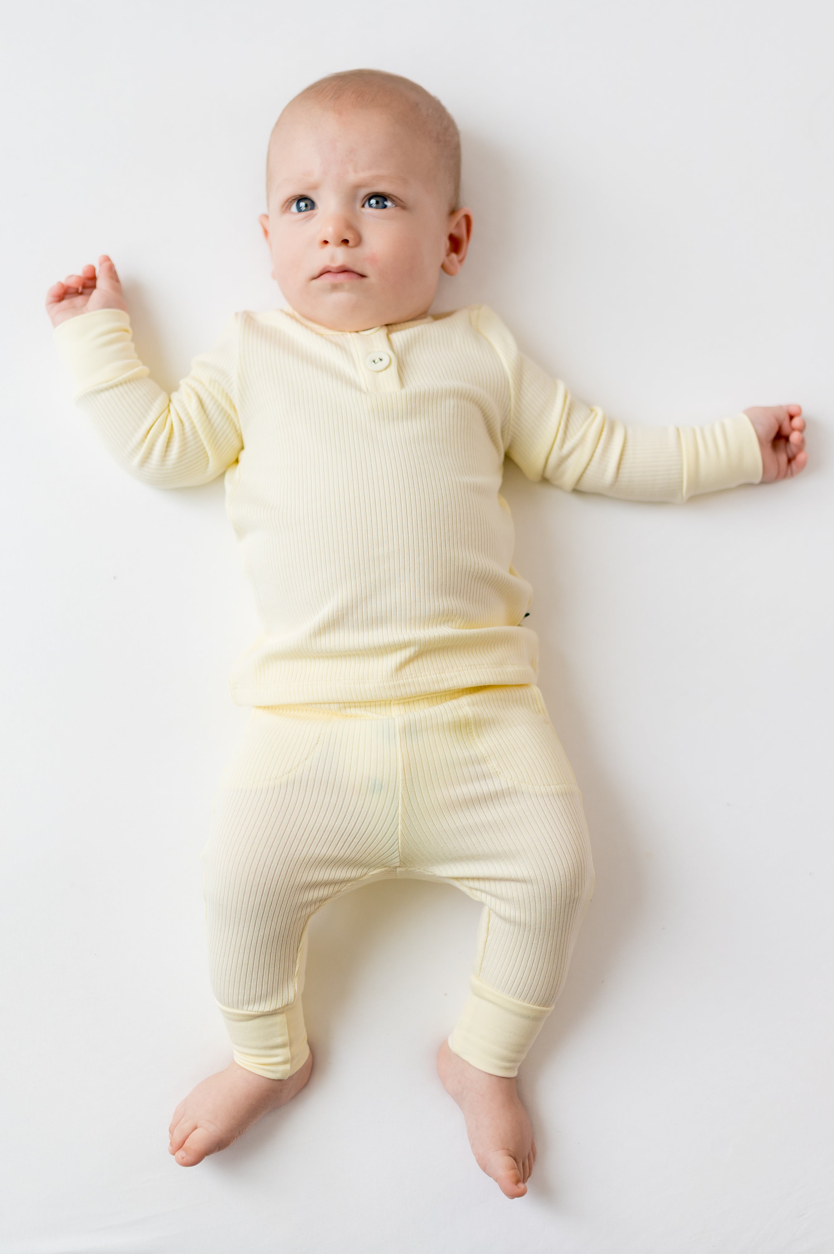Infant laying on a white surface wearing the Ribbed Infant Henley Set in Chamomile