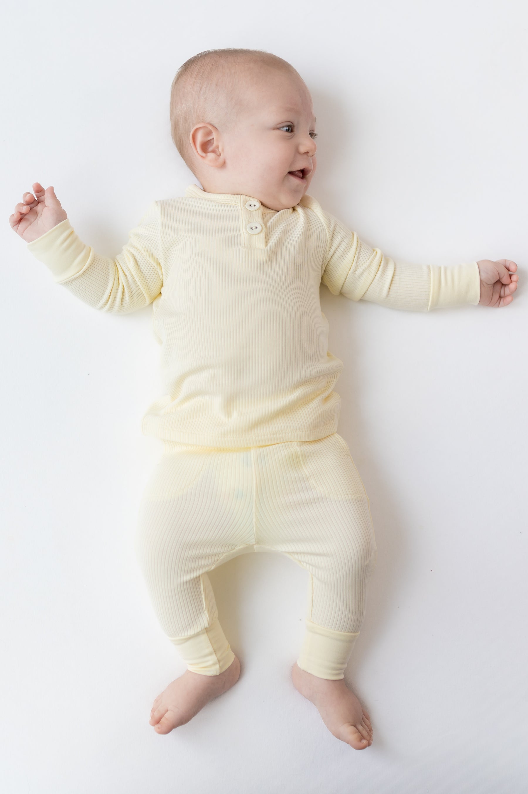 Smiling infant laying on a white surface wearing the Ribbed Infant Henley Set in Chamomile