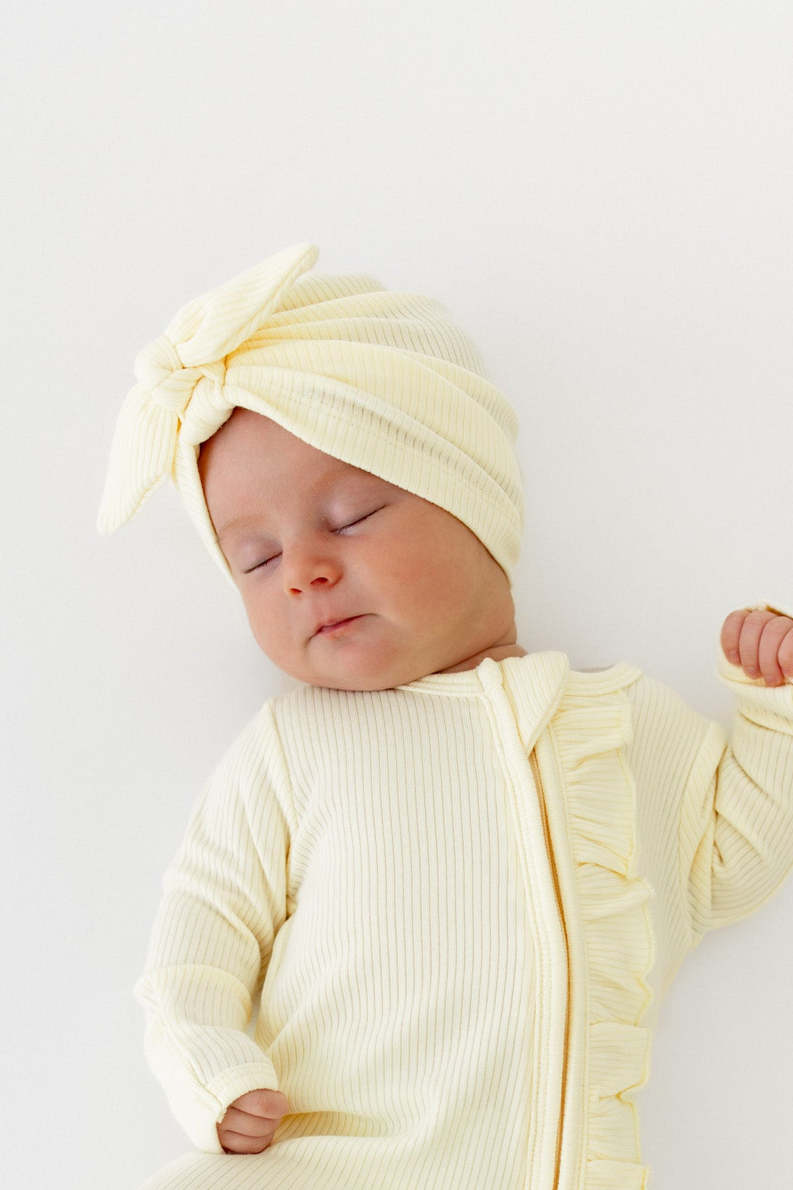 Close up of a newborn wearing the Ribbed Headwrap in Chamomile with matching ribbed ruffle zipper romper