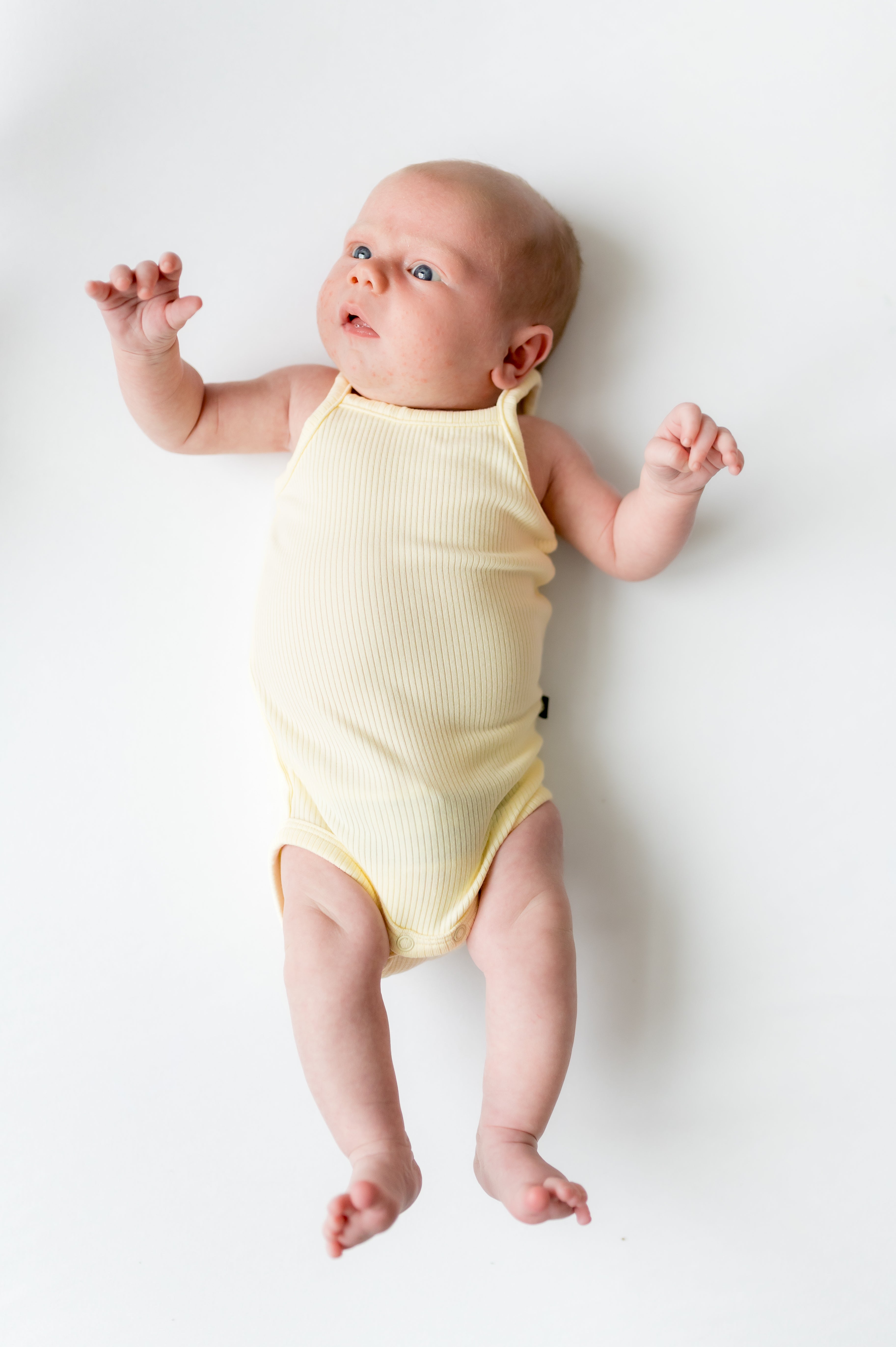 Newborn laying on a white surface looking up wearing the Ribbed Spaghetti Strap Bodysuit in Chamomile