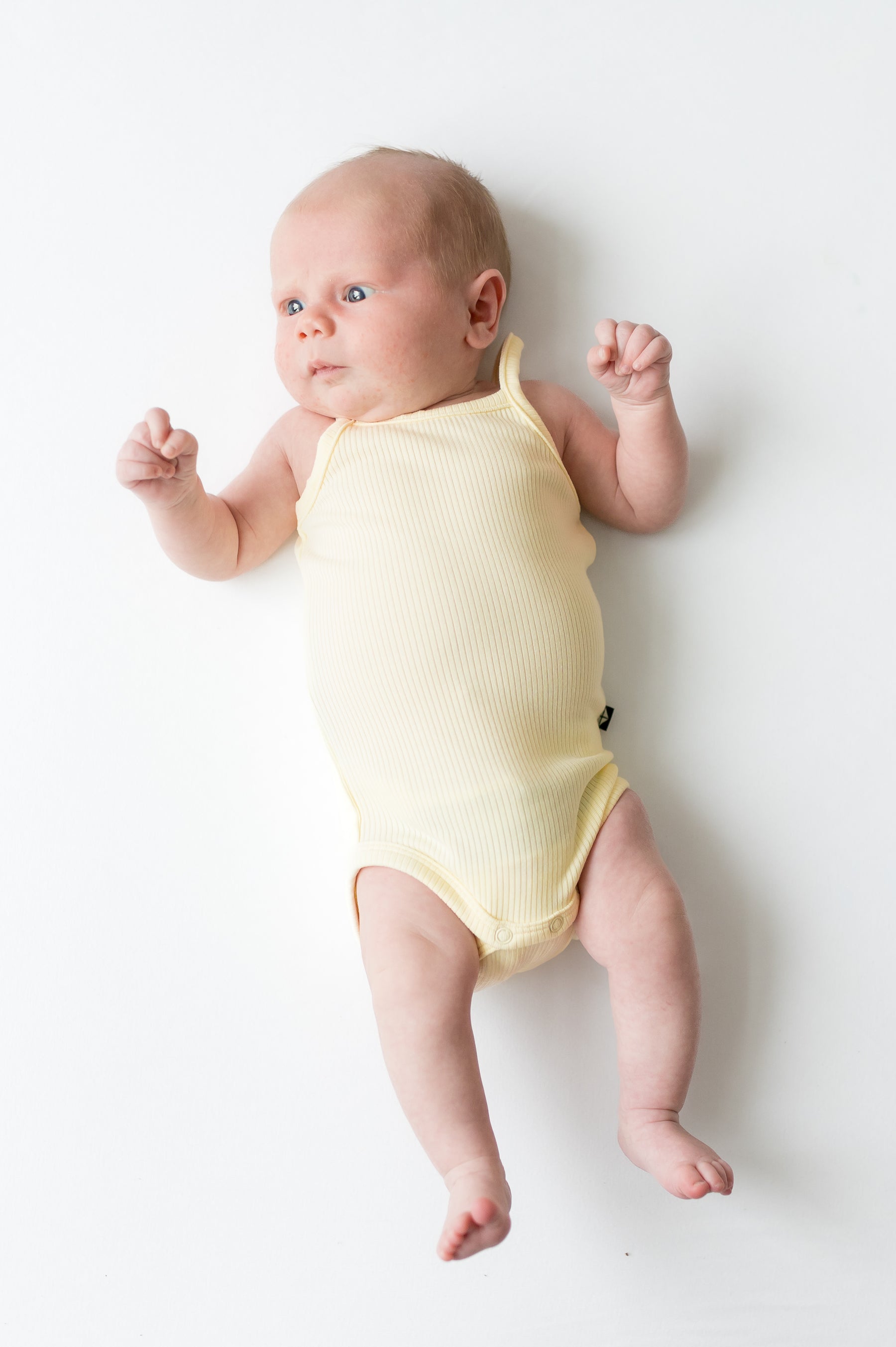 Newborn laying on a white surface wearing the Ribbed Spaghetti Strap Bodysuit in Chamomile