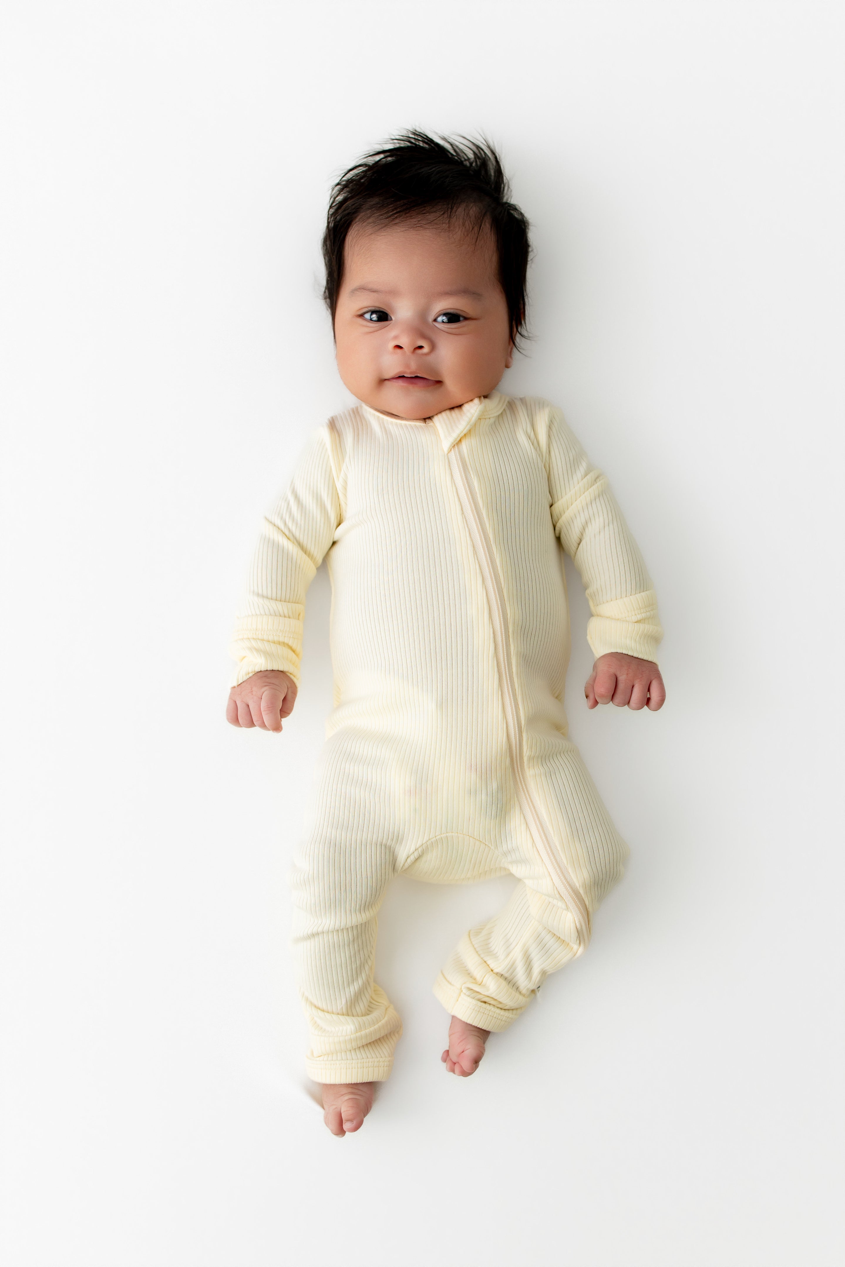 Newborn laying on a white surface wearing the Ribbed Zipper Romper in Chamomile