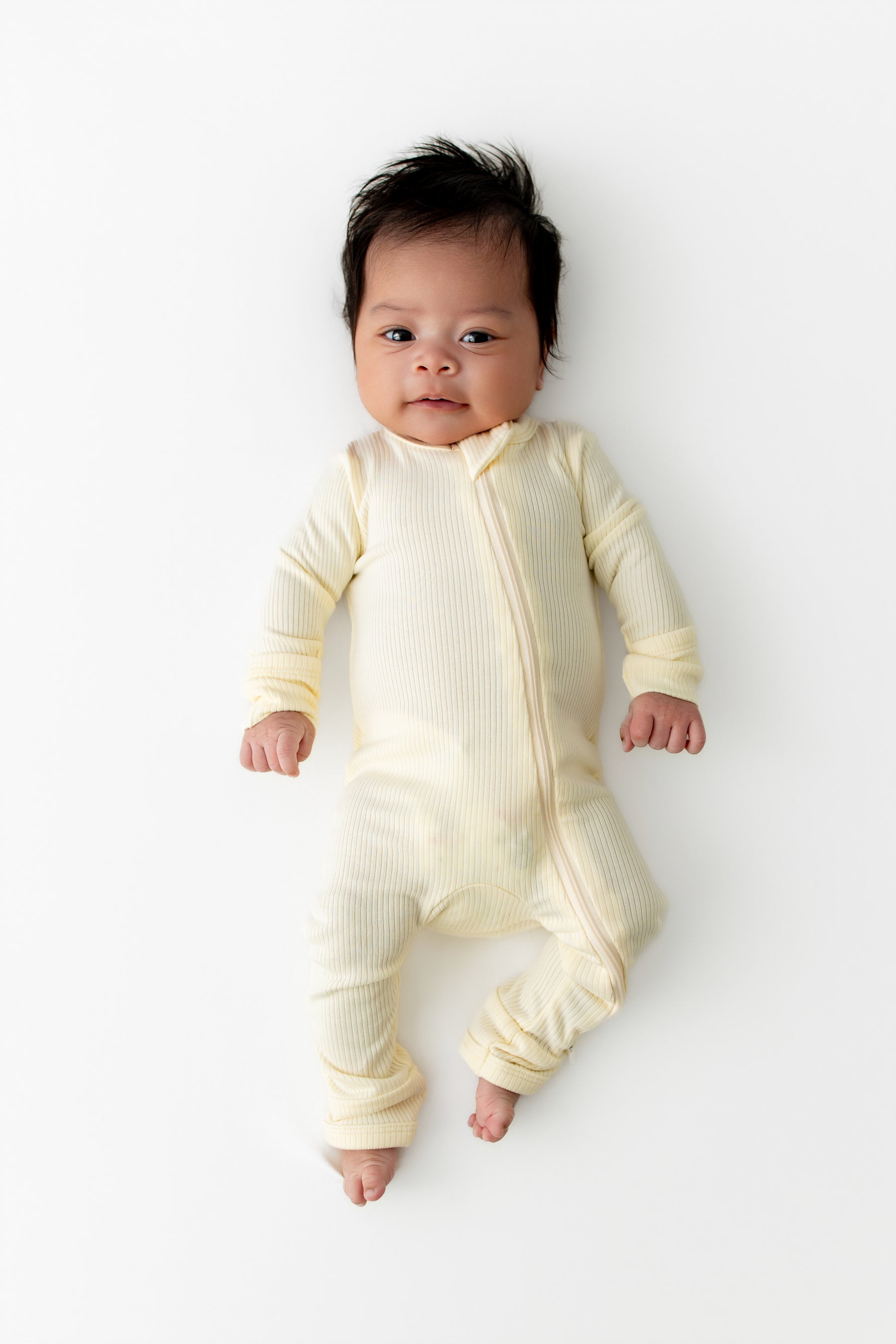 Newborn laying on a white surface wearing the Ribbed Zipper Romper in Chamomile