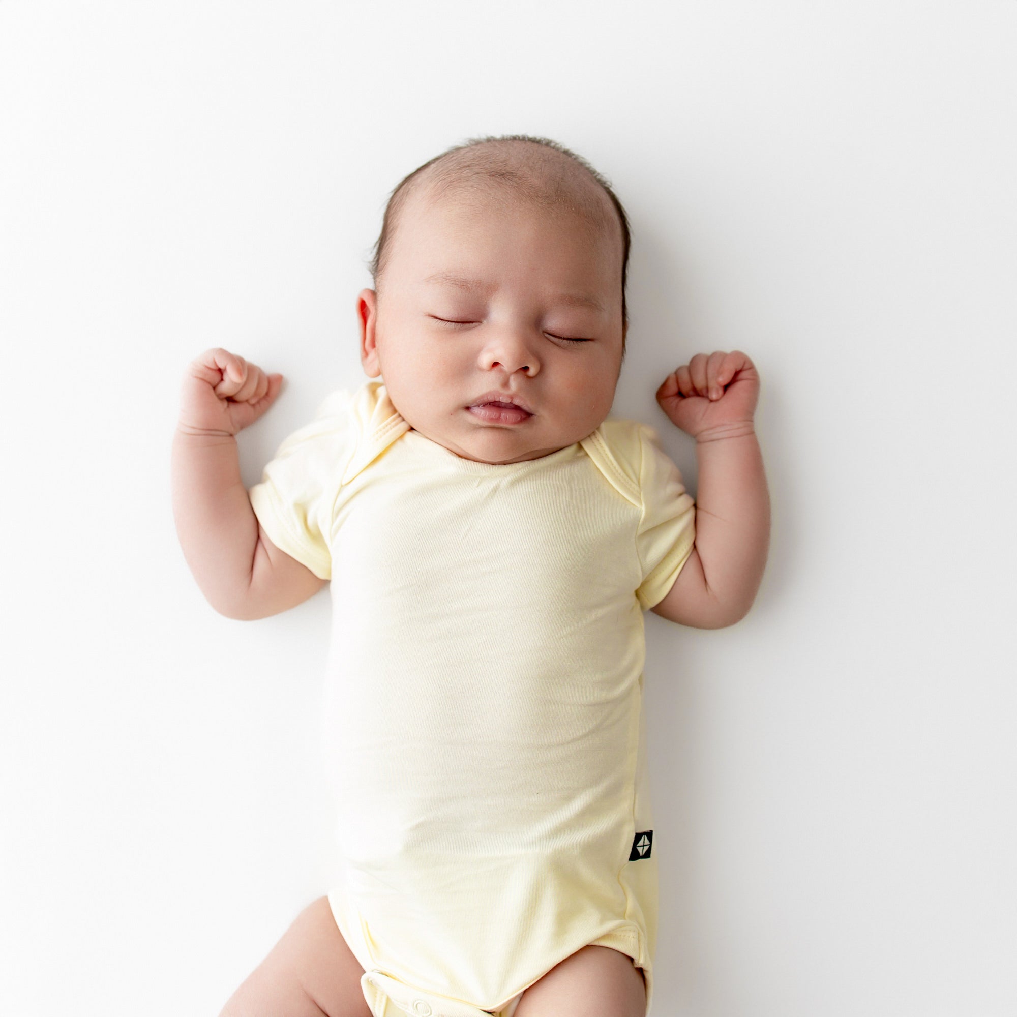 Baby in a yellow onesie lying on a white surface