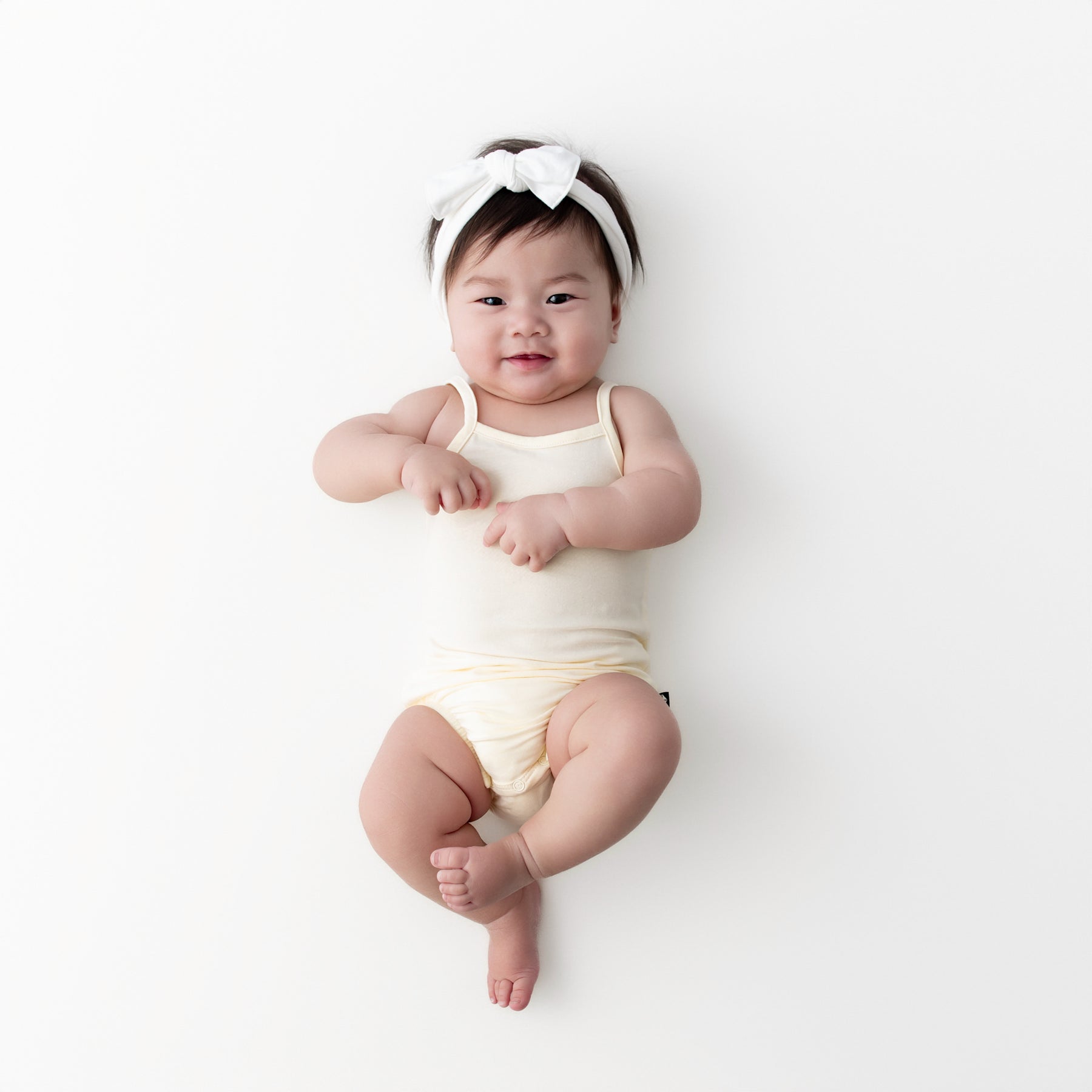 Infant wearing the Spaghetti Strap Leotard in Chamomile laying on a neutral surface
