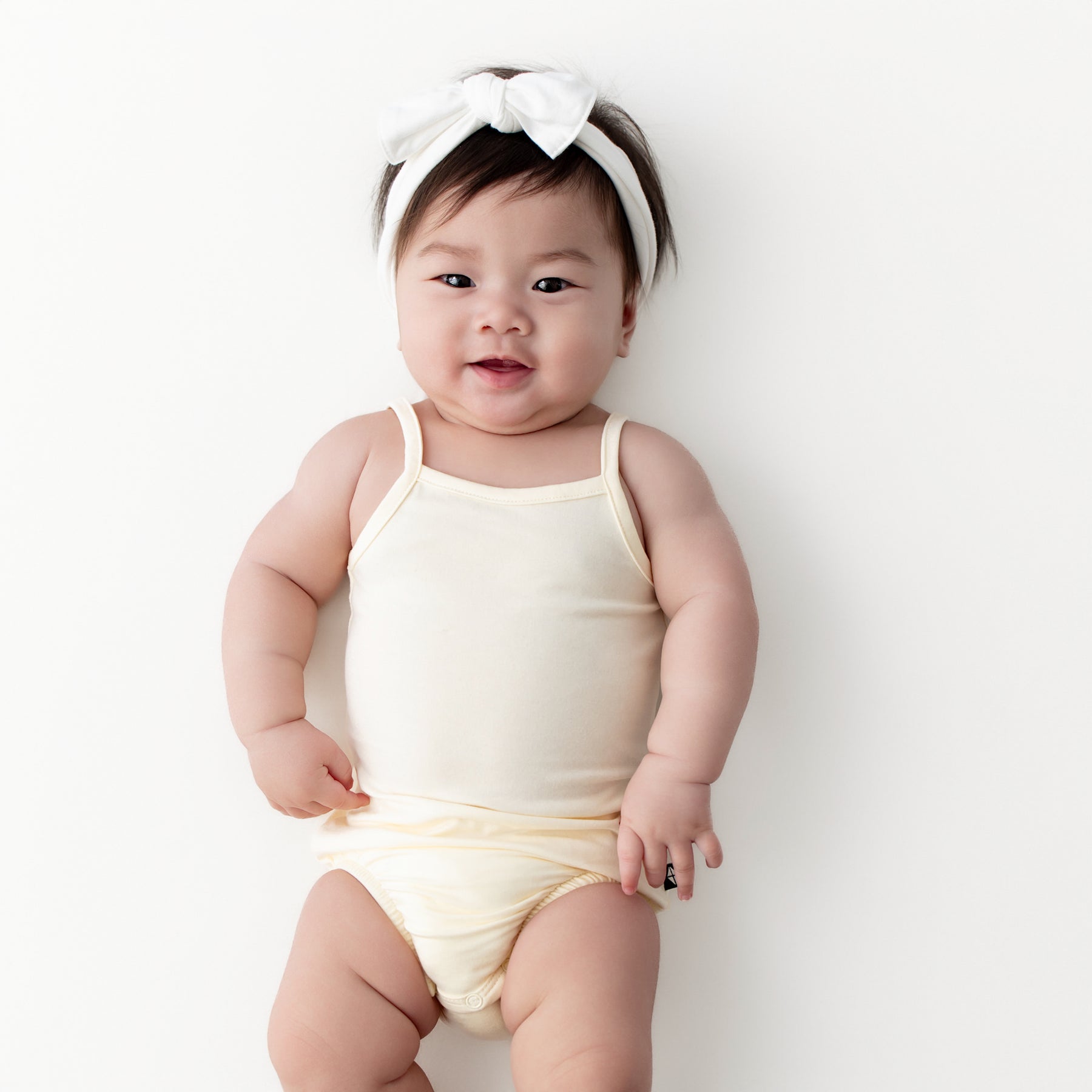 Infant girl laying on a light neutral surface wearing the Spaghetti Strap Leotard in Chamomile