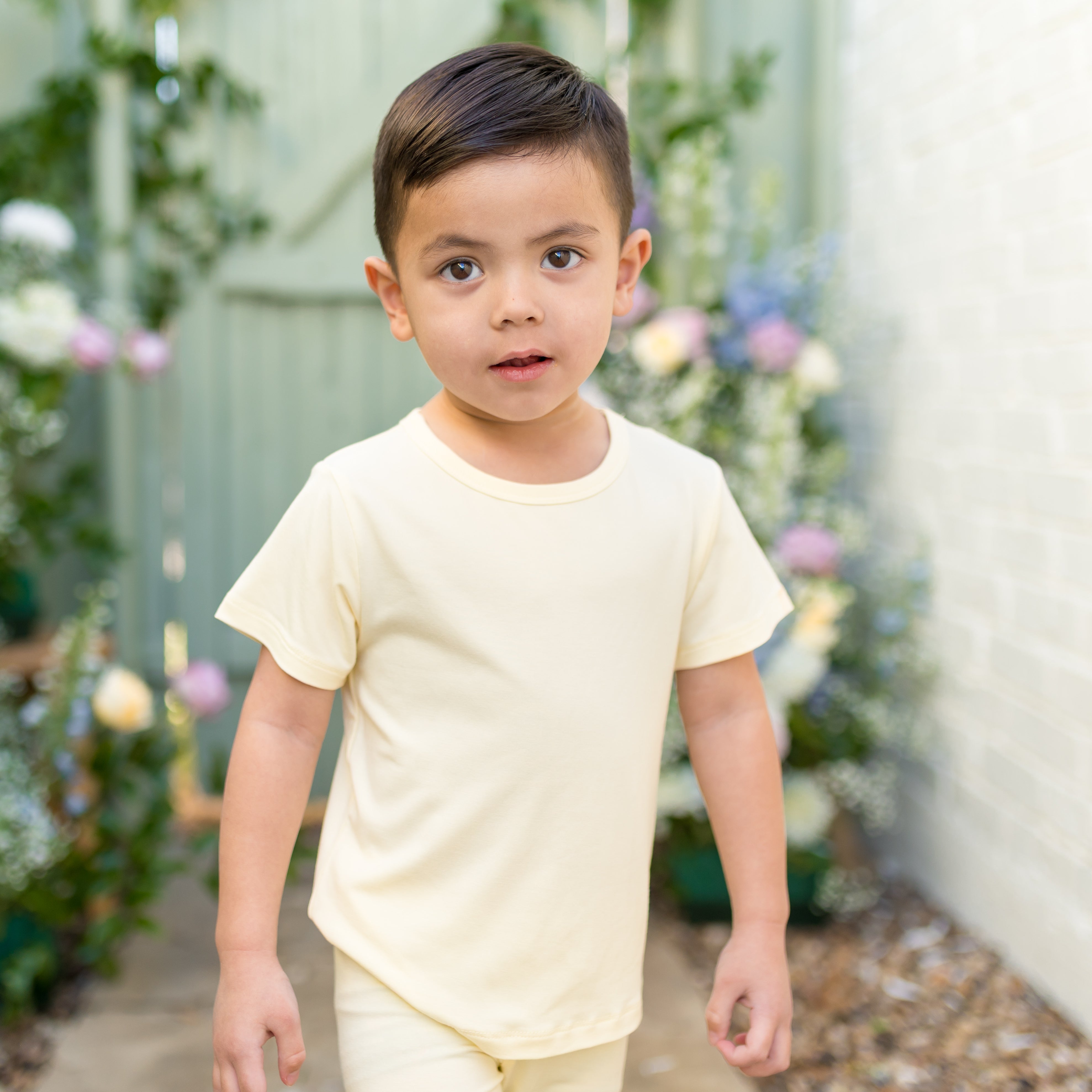 Child wearing a pale yellow short sleeve tshirt with an outdoor setting background