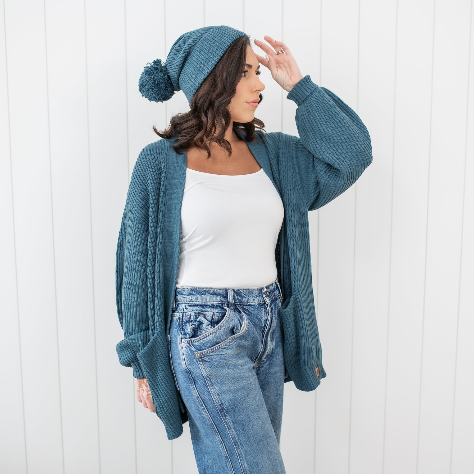 Close up of female model wearing the Chunky Knit Women's Oversized Cardigan in Atlantic with a matching chunky knit pom beanie 