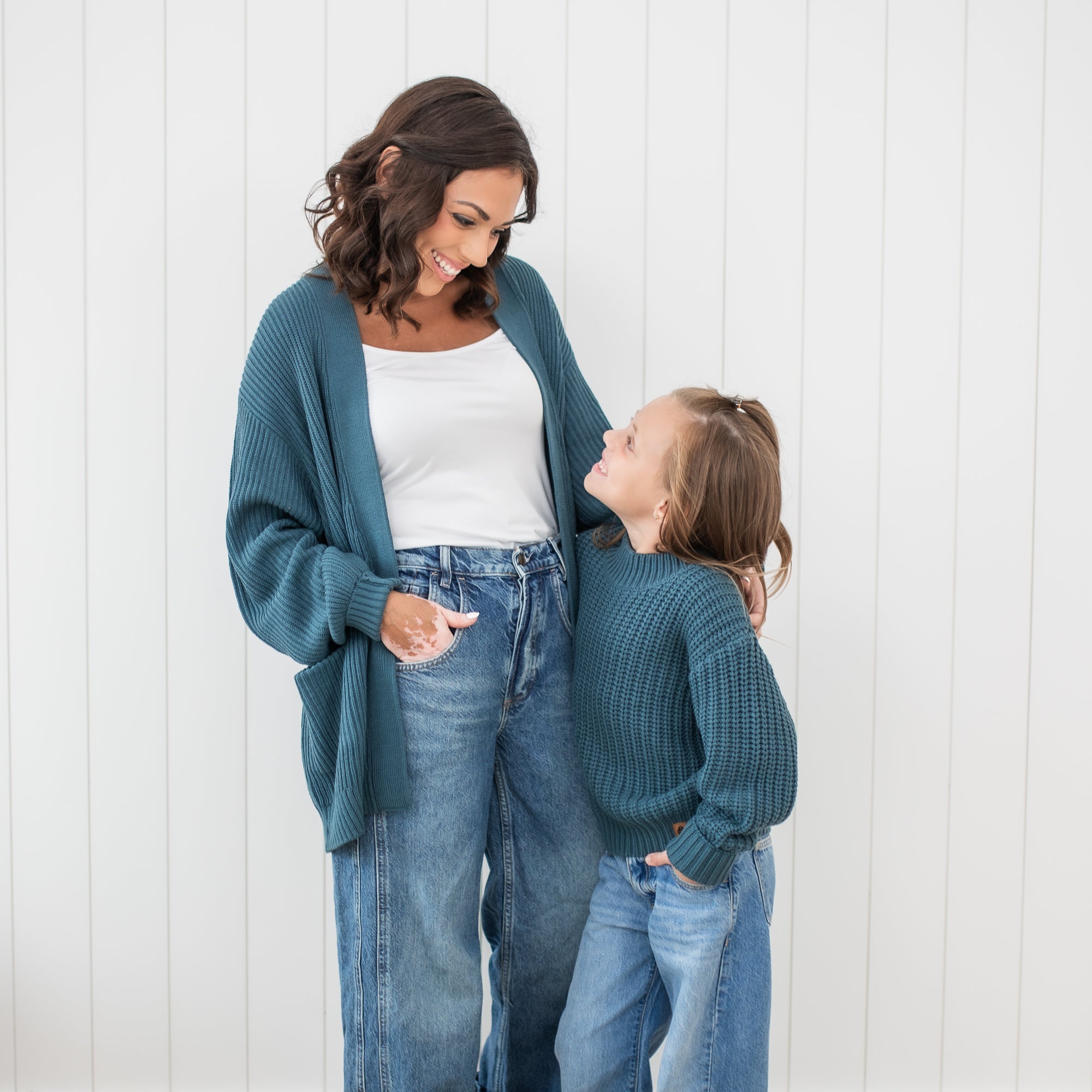 Mother and daughter standing looking at one another wearing the Chunky Knit Women's Oversized Cardigan in Atlantic and Chunky knit sweater in atlantic