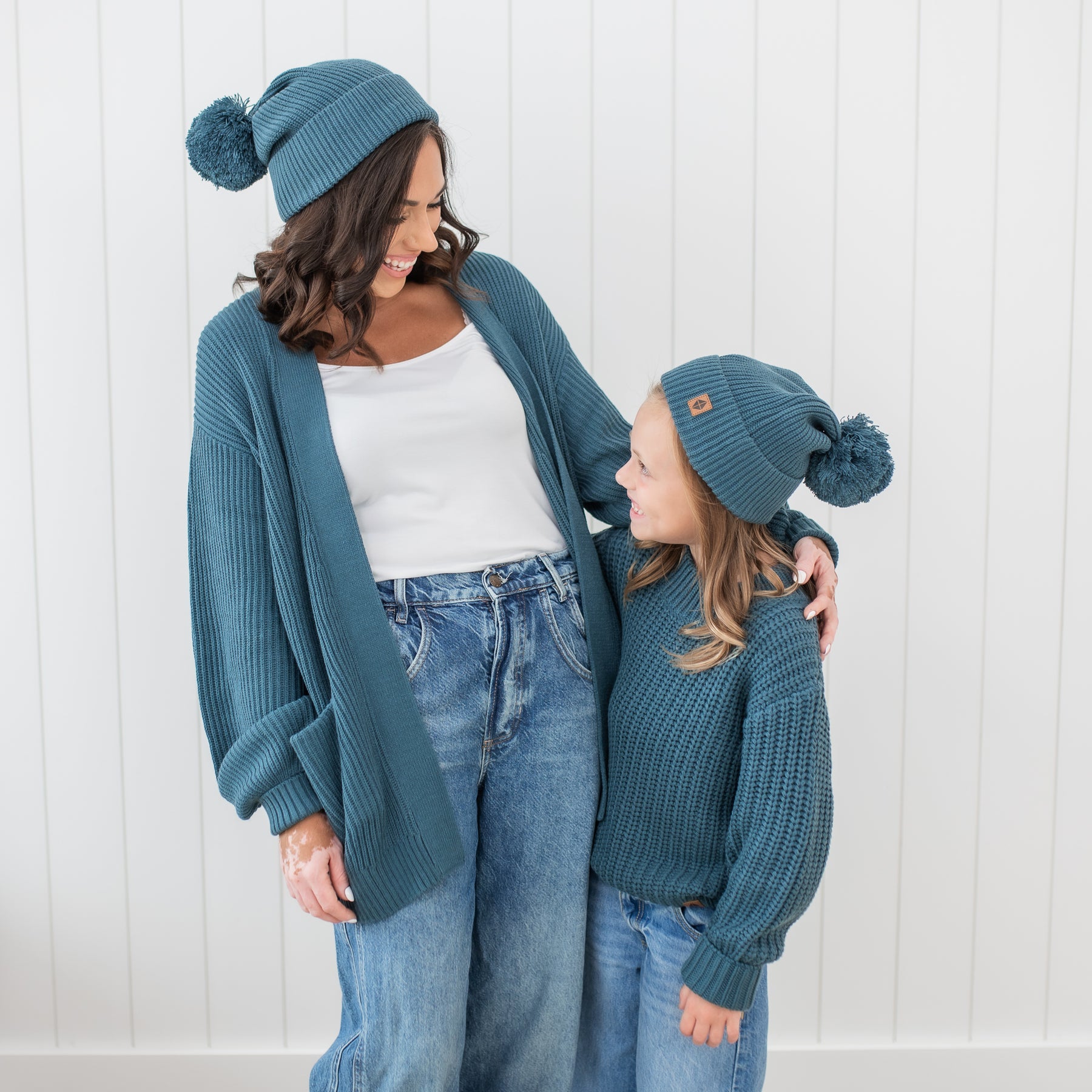Mother and daughter wearing matching Chunky Knit items in Atlantic. Pictured are the Chunky Knit Adult Pom Beanie in Atlantic, Chunky Knit Women's Oversized cardigan, chunky knit sweater and chunky knit pom beanie