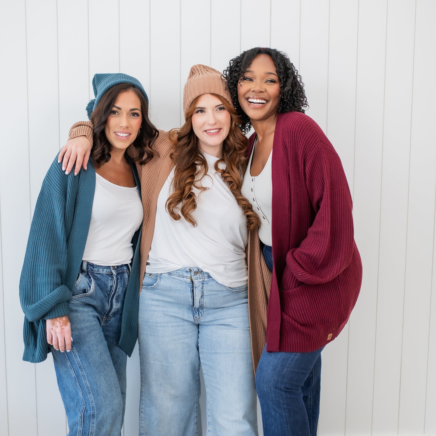 Three female models standing side by side wearing the Chunky Knit Women's Oversized Cardigan in Atlantic, Latte and Burgundy