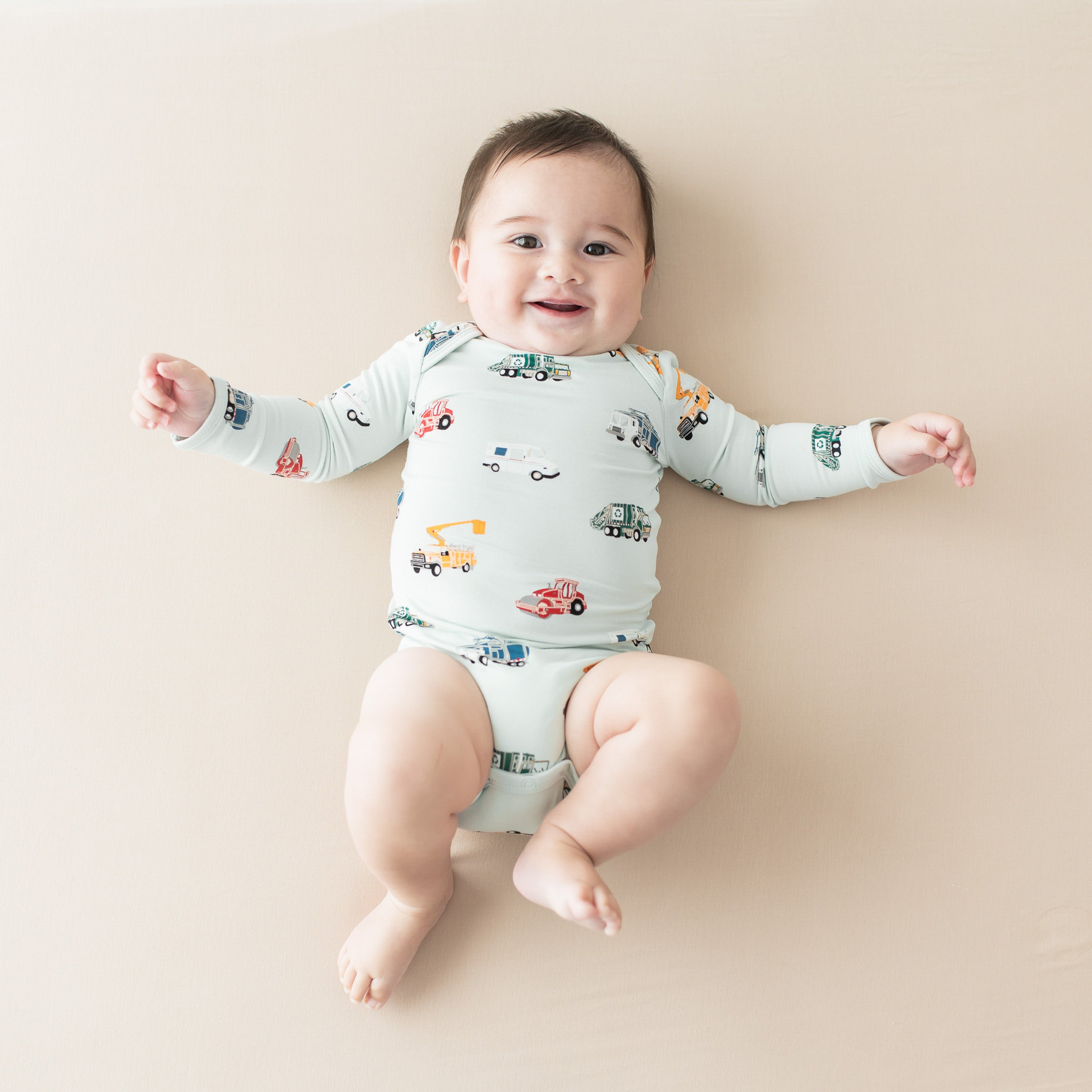 Infant laying on a light beige surface wearing the Long Sleeve Bodysuit in City Vehicles