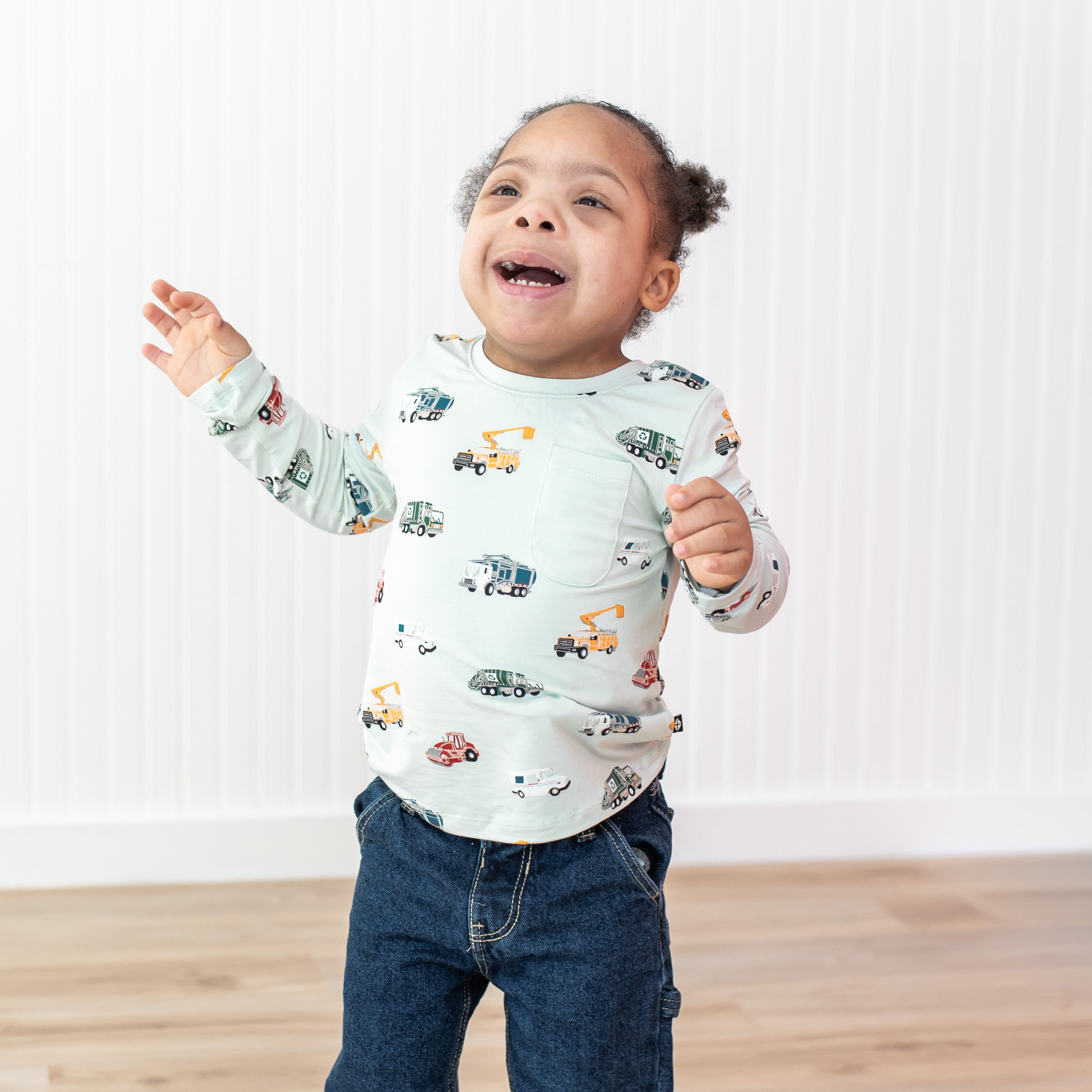 Smiling toddler walking wearing the Long Sleeve Toddler Crew Neck Tee in City Vehicles with medium wash jeans