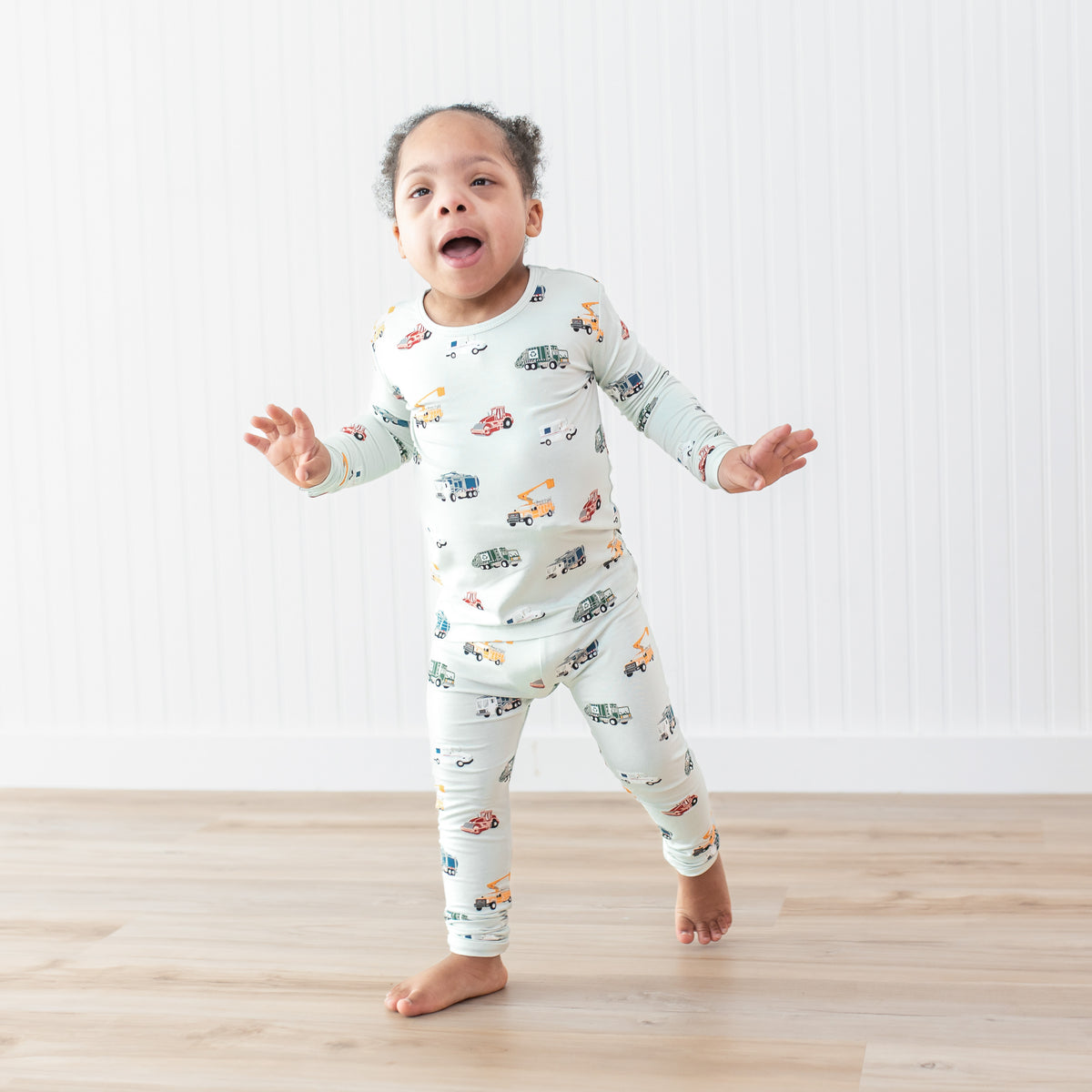 Young child walking on a wood floor in front of a white paneled wall wearing the soft and breathable Long Sleeve Pajamas in City Vehicles