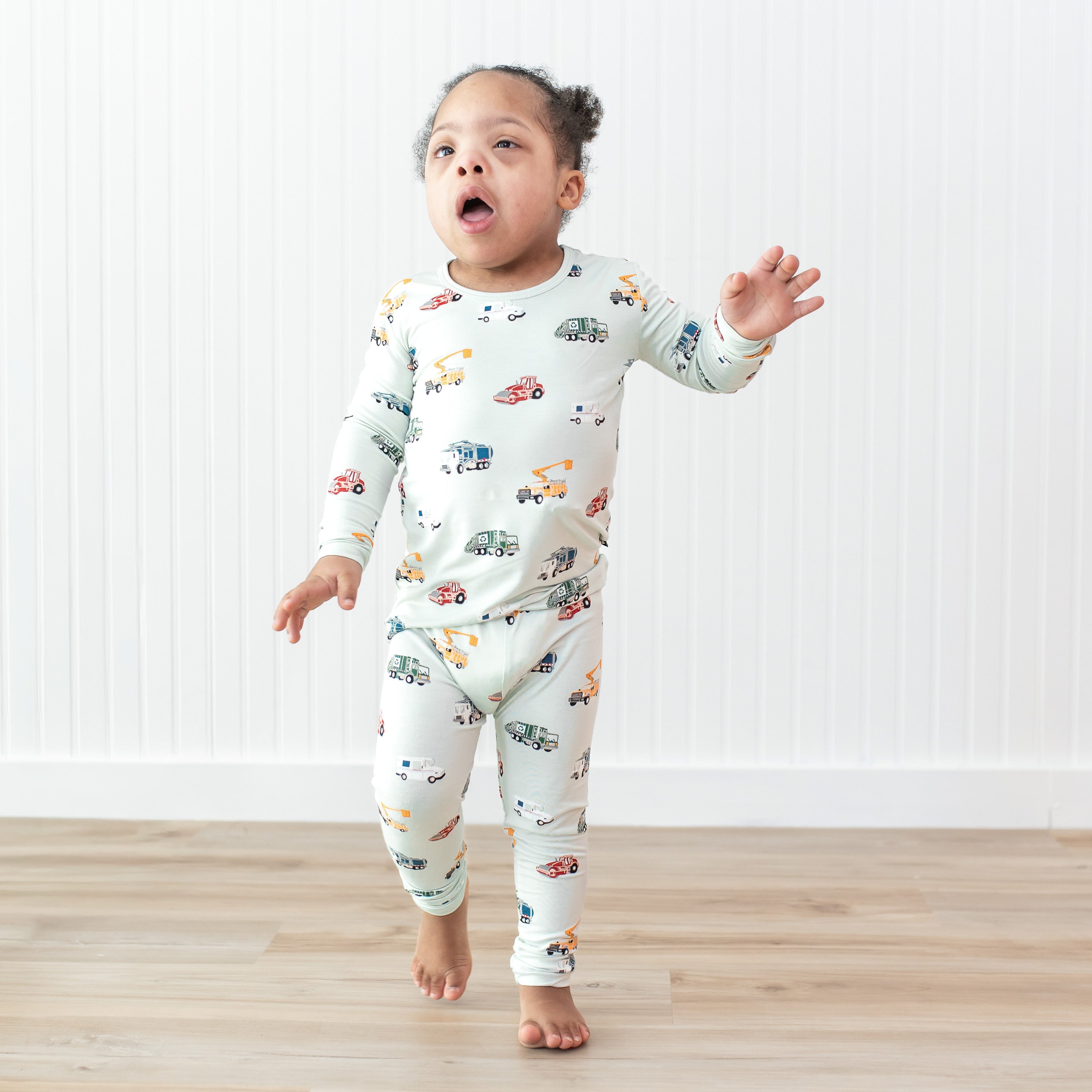 Young child walking in front of a white paneled wall wearing the Long Sleeve Pajamas in City Vehicles