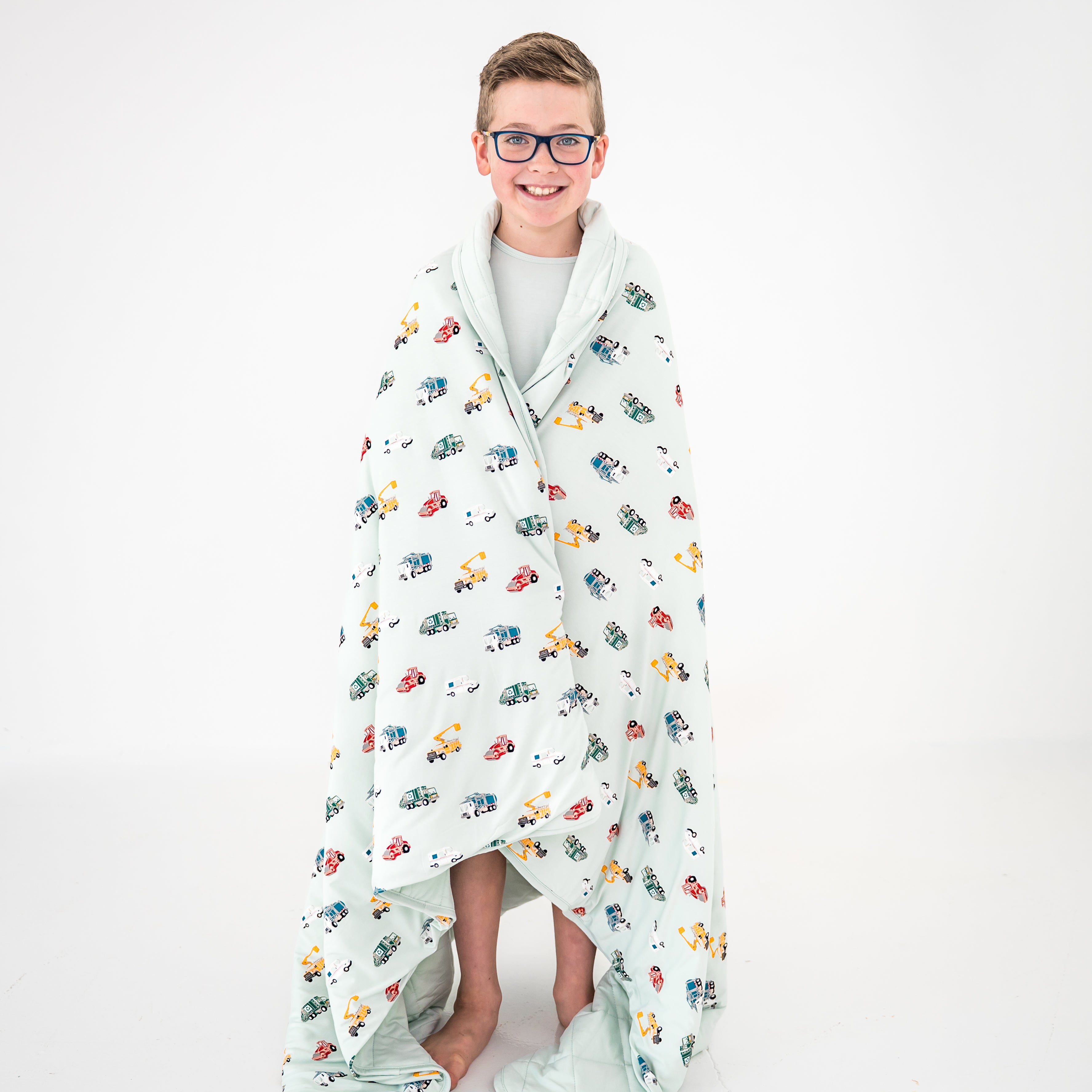 Young boy standing in front of a white background with the Youth Blanket in City Vehicles 2.5 around his shoulders
