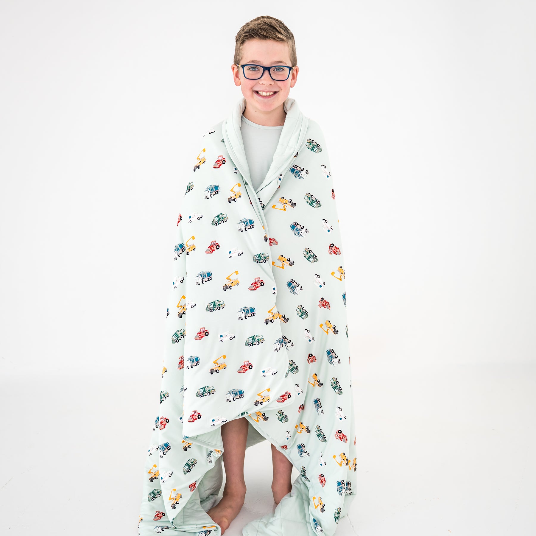 Young boy standing in front of a white background with the Youth Blanket in City Vehicles 2.5 around his shoulders