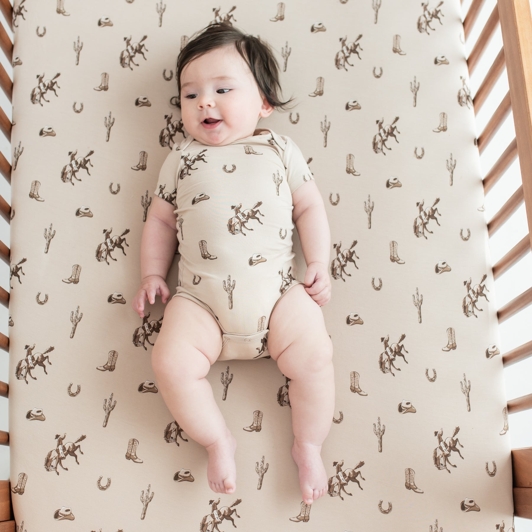 Infant laying in a crib on a Crib Sheet in Classic Cowboy wearing a matching short sleeve bodysuit